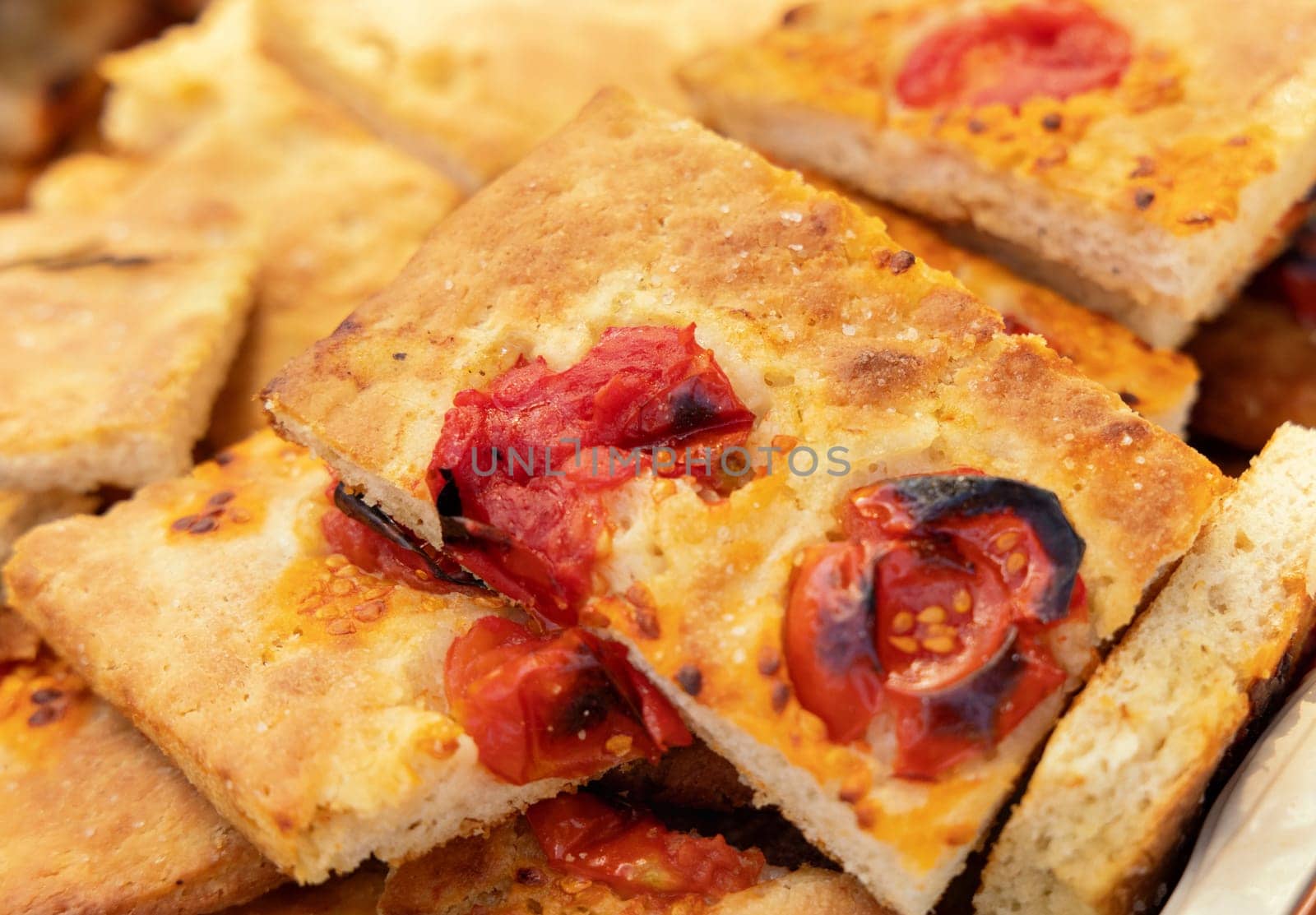 Freshly baked homemade apulian focaccia cut in slices close up. Barese focaccia with tomatoes, extra virgin olive oil and salt flakes. Italian Mediterranean traditional food