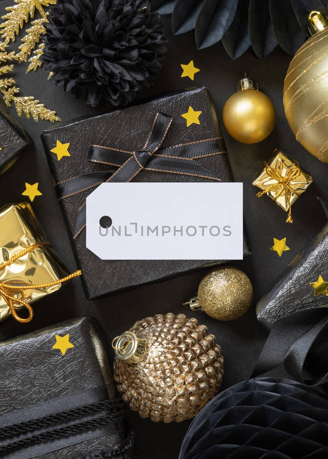 Black and golden Christmas Gift Boxes with a bow and ornaments close up, horizontal paper gift tag mockup, copy space. Dark winter composition with blank label card for Christmas, New Year, Birthday, Anniversary