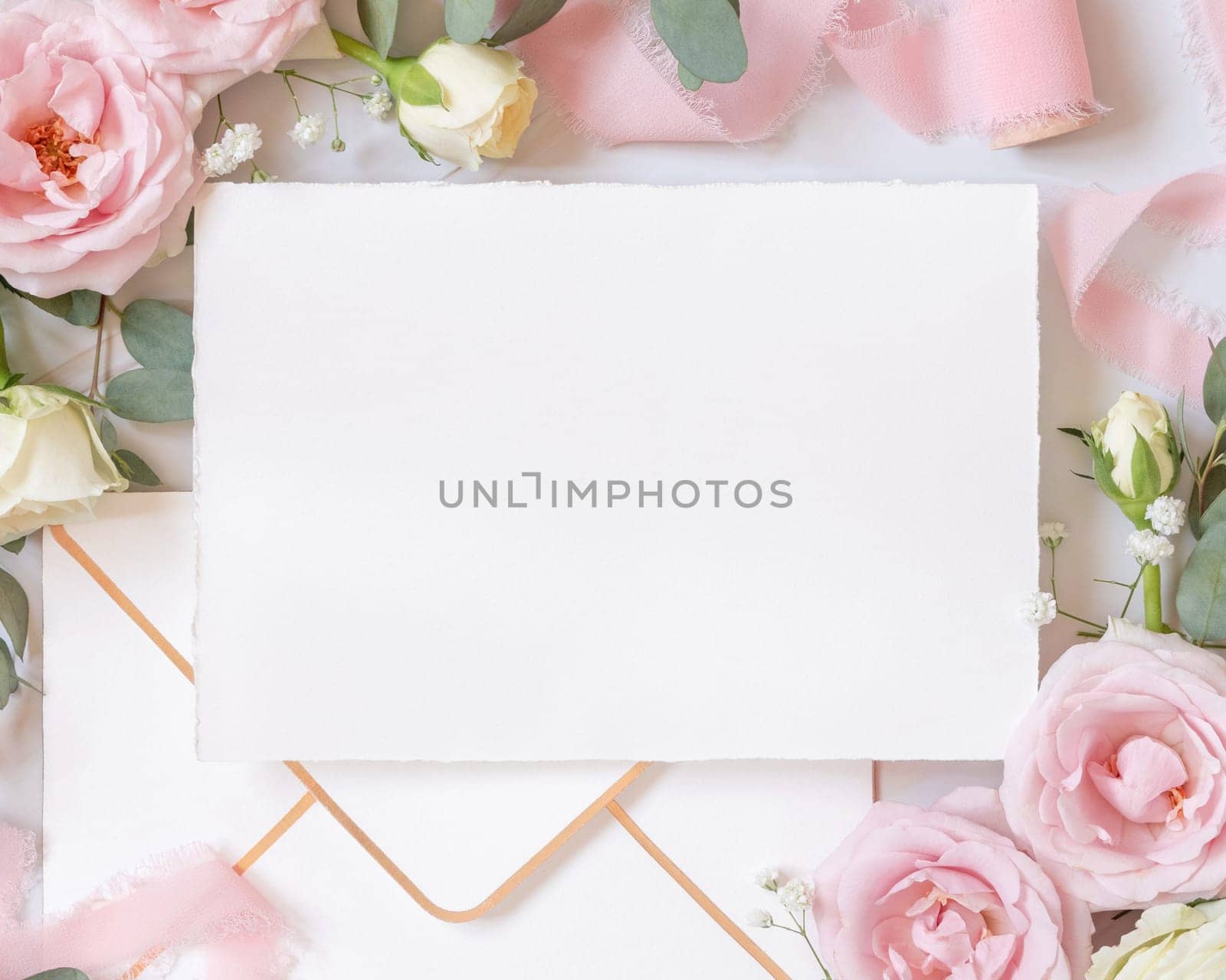Paper card and envelope between light pink roses and silk ribbons on marble top view, wedding mockup. Romantic scene with blank card and pastel flowers flat lay. Valentines, Spring or Mothers day