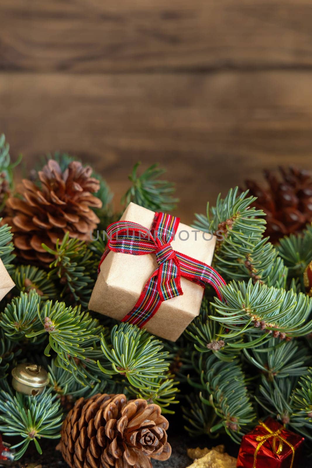 Wrapped gift boxes on reen fir branches near Christmas decorations and pine cones close up on wooden background, copy space. Christmas or New Year Holiday atmosphere