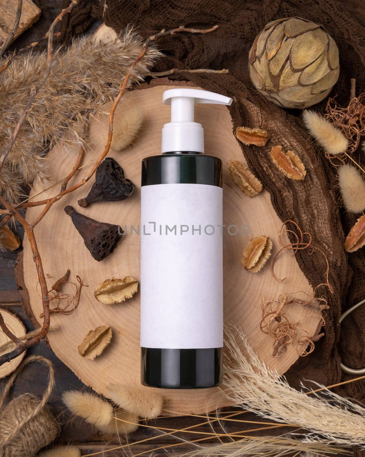 Refillable one pump bottle on wood near natural boho decorations top view, label mockup. Skincare beauty product, lotion or essence. Bohemian eco friendly cosmetics flat lay with dried leaves.