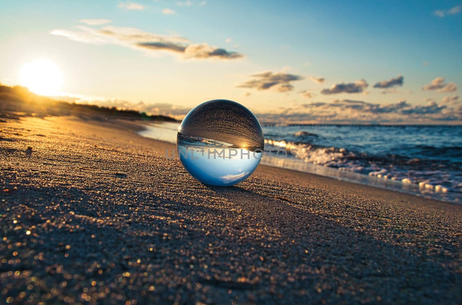 Glass globe on the beach of the Baltic Sea in Zingst in which the landscape is depicted. The sunset provides a warm light mood