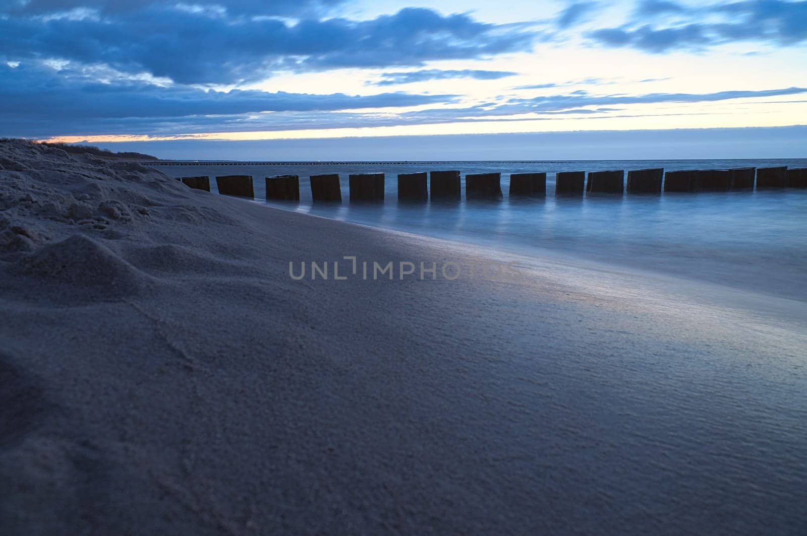 sunset on the beach of the Baltic Sea. Groynes reach into the sea. blue hour with clouds in the sky. Landscape photo in Zingst