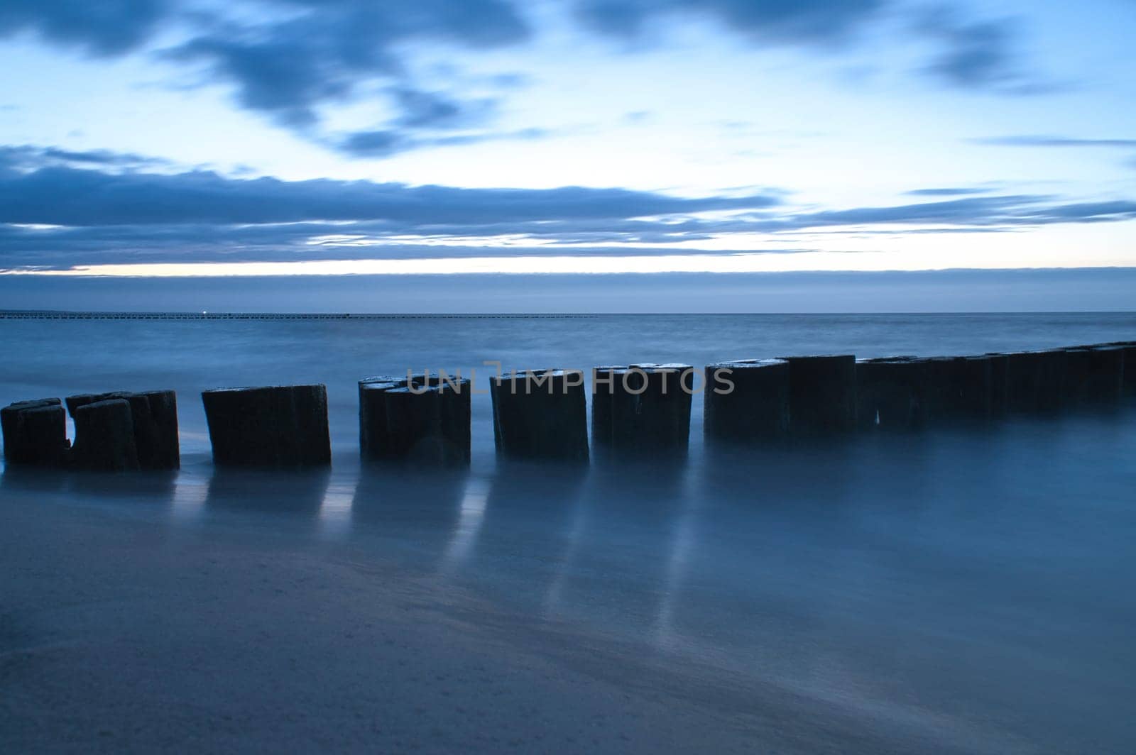 sunset on the beach of the Baltic Sea. Groynes reach into the sea. blue hour with clouds in the sky. Landscape photo in Zingst