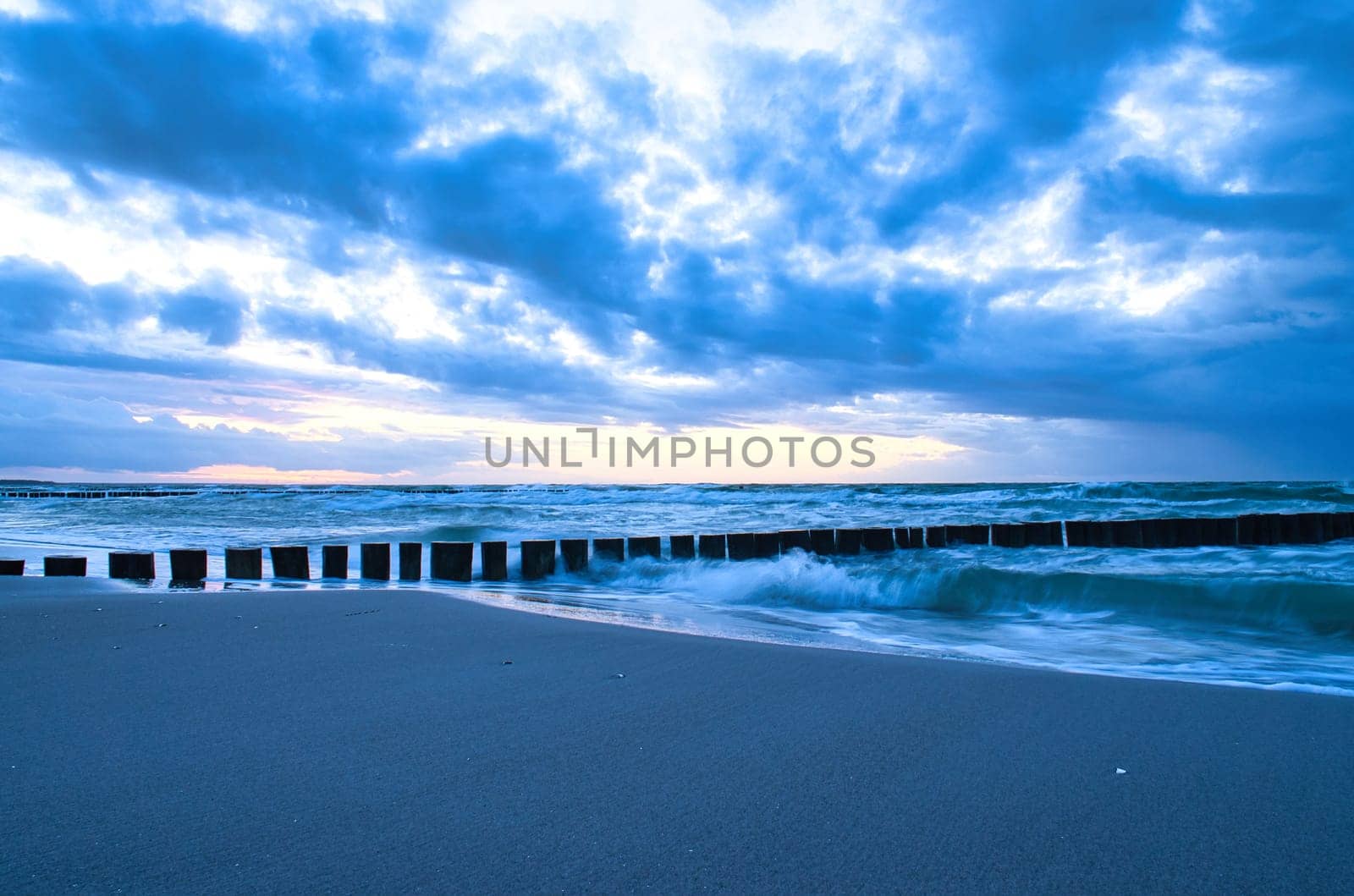 sunset on the beach of the Baltic Sea. Groynes reach into the sea. blue hour with clouds in the sky. Landscape photo in Zingst