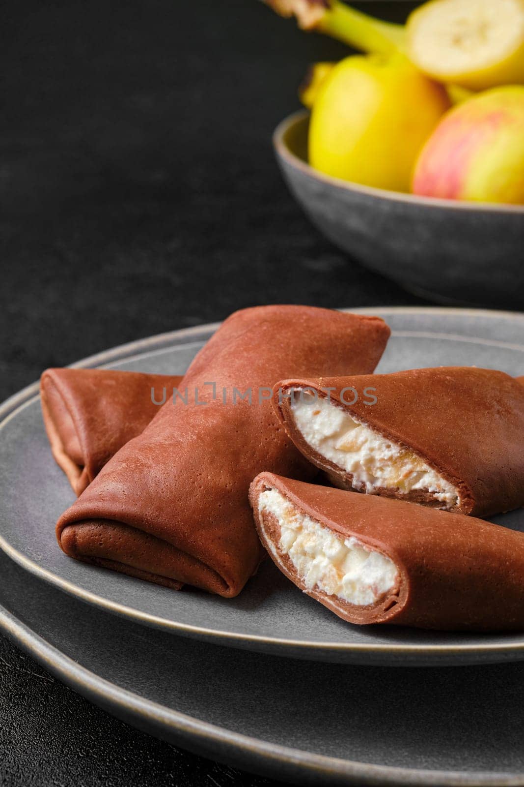 Closeup view of thin chocolate pancakes stuffed with curd, banana and apple