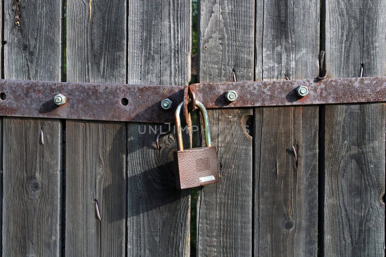 Padlock brown metal lock close-up on old gray wooden gate