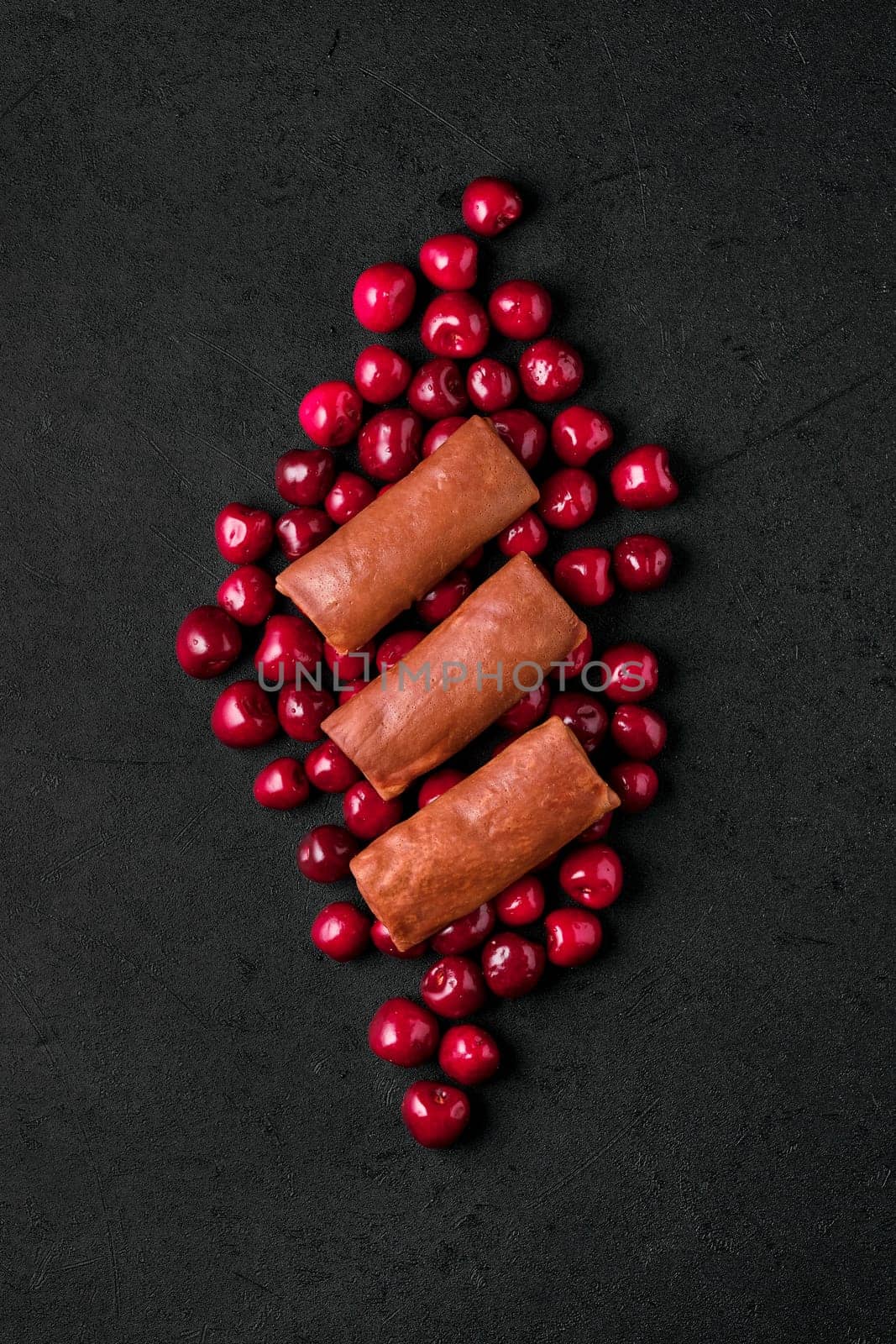 Overhead composition with thin chocolate pancakes stuffed with curd, blueberry and cherry