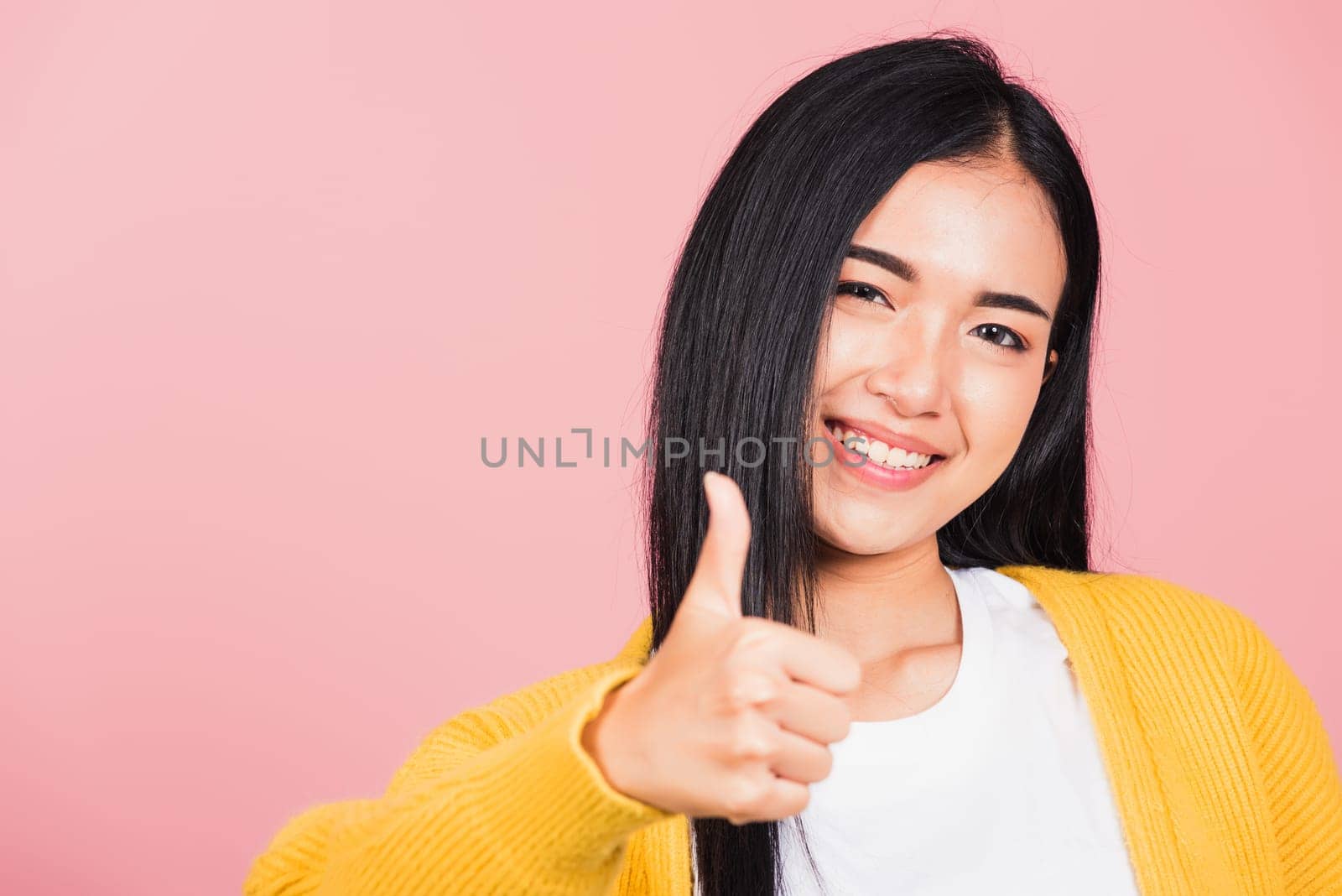 .Portrait Asian beautiful young woman smile she standing made finger thumbs up, Ok sign to agree studio shot isolated on pink background, Thai female successful like finger gesture with copy space