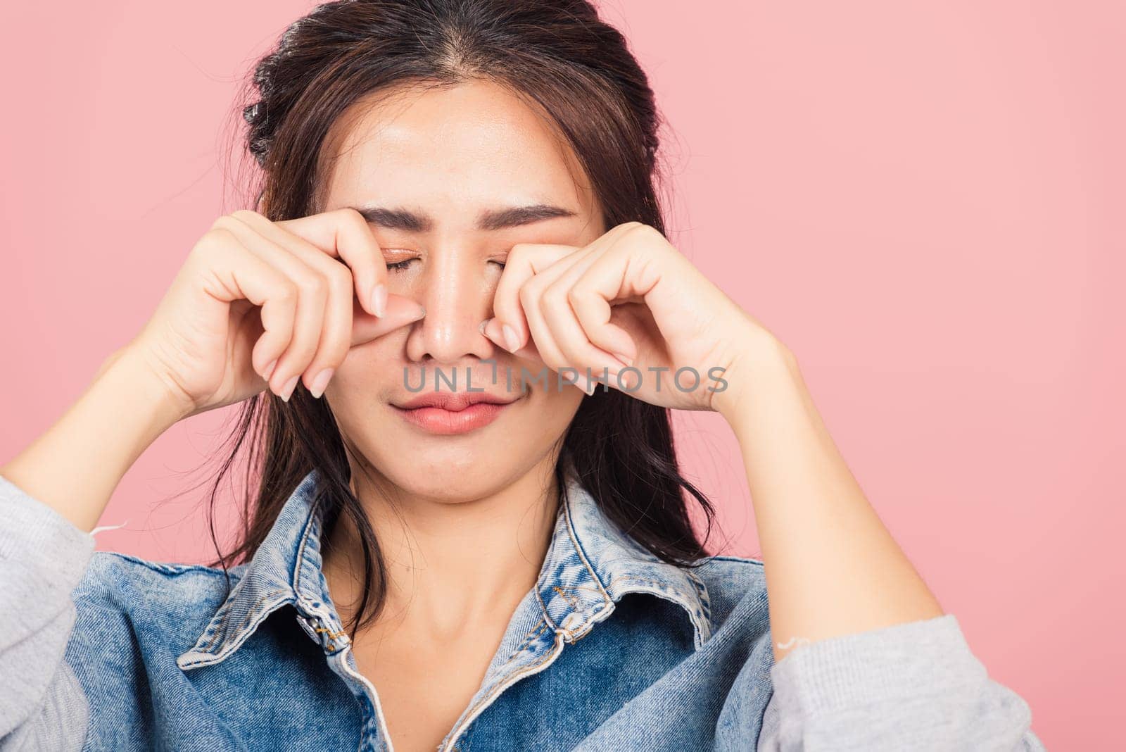 Asian portrait beautiful cute young woman wear denim bad mood her cry wipe tears with fingers, studio shot isolated on pink background, Thai female feeling sad unhappy crying with copy space