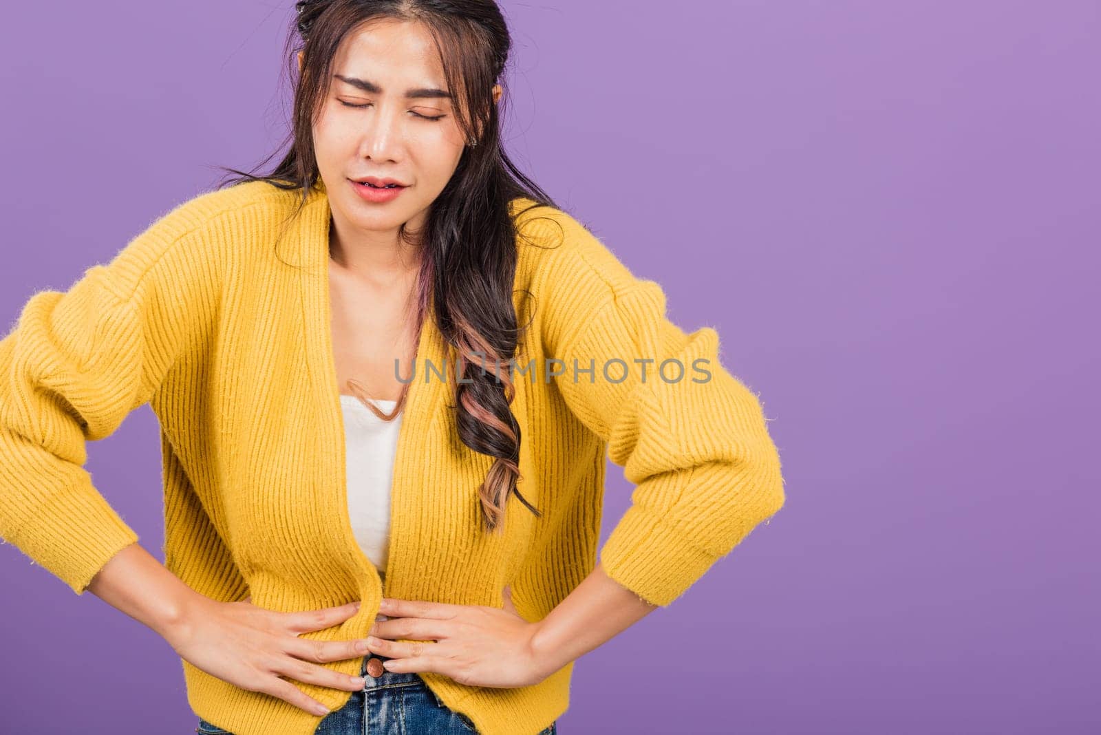 Portrait of Asian beautiful young woman has stomachache, female abdominal pain suffering from stomach ache, studio shot isolated on purple background, Health and medical gastritis concept