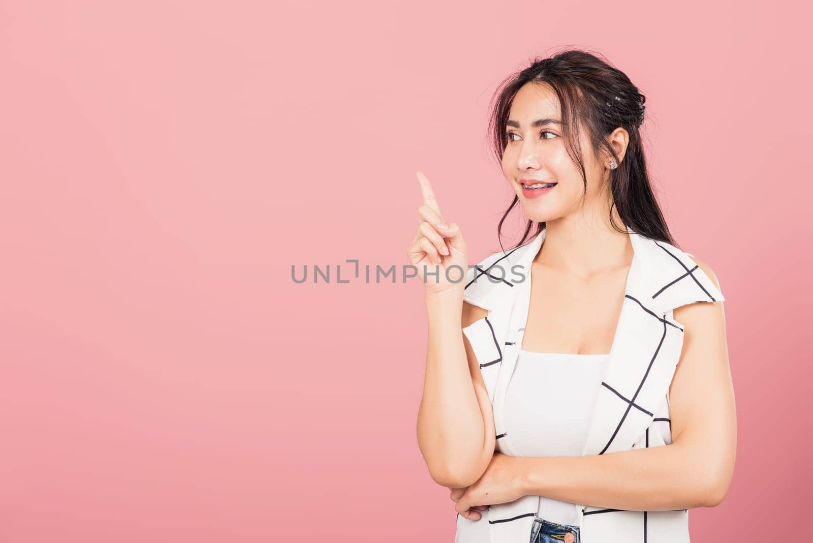 Happy Asian portrait beautiful cute young woman standing smiling indicate finger empty space looking to space, studio shot isolated on pink background, Thai female pointing index out with copy space