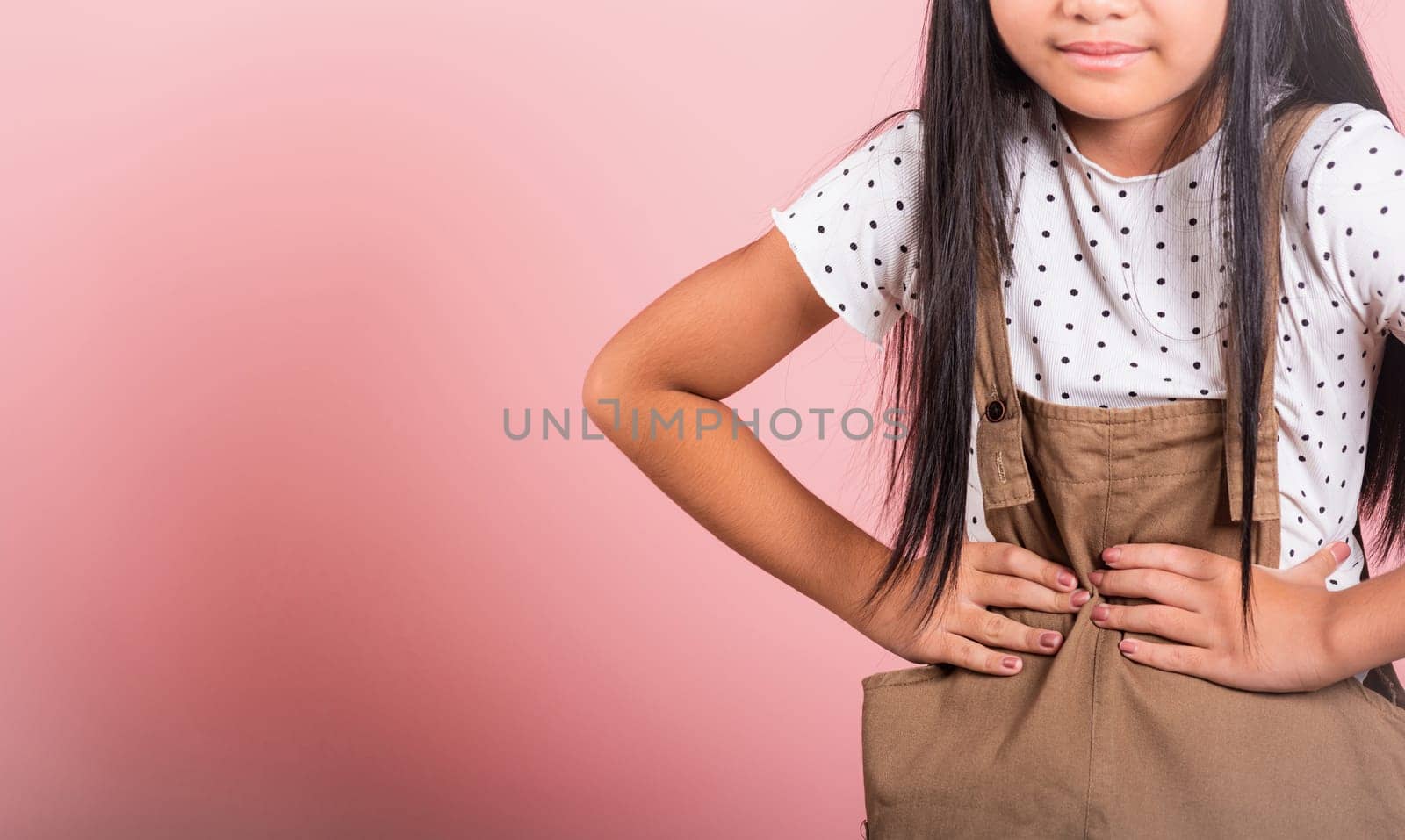 Asian little kid 10 years old suffering from stomach ache at studio shot isolated on pink background, Happy child girl hand hold stomach pain because indigestion, painful illness feeling unwell