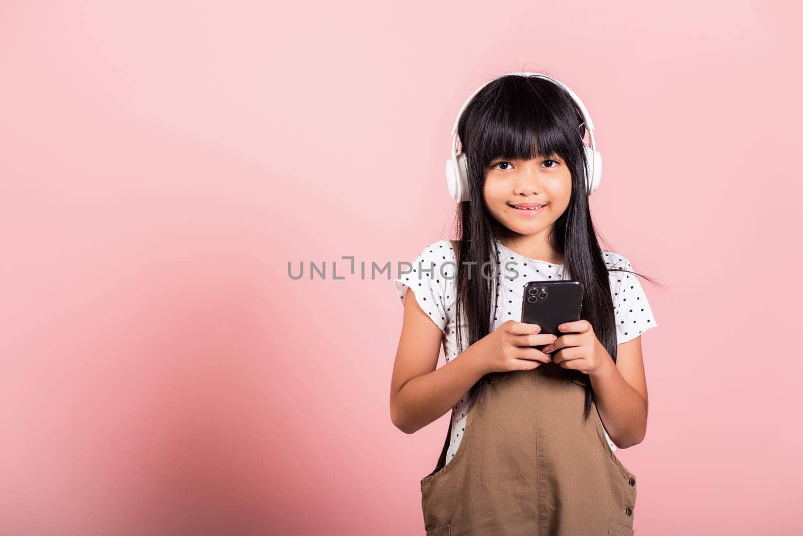 Asian kid 10 years enjoying listening music from mobile phone wear wireless headset at studio shot isolated on pink background, Happy child girl lifestyle use smartphone listen music with headphones