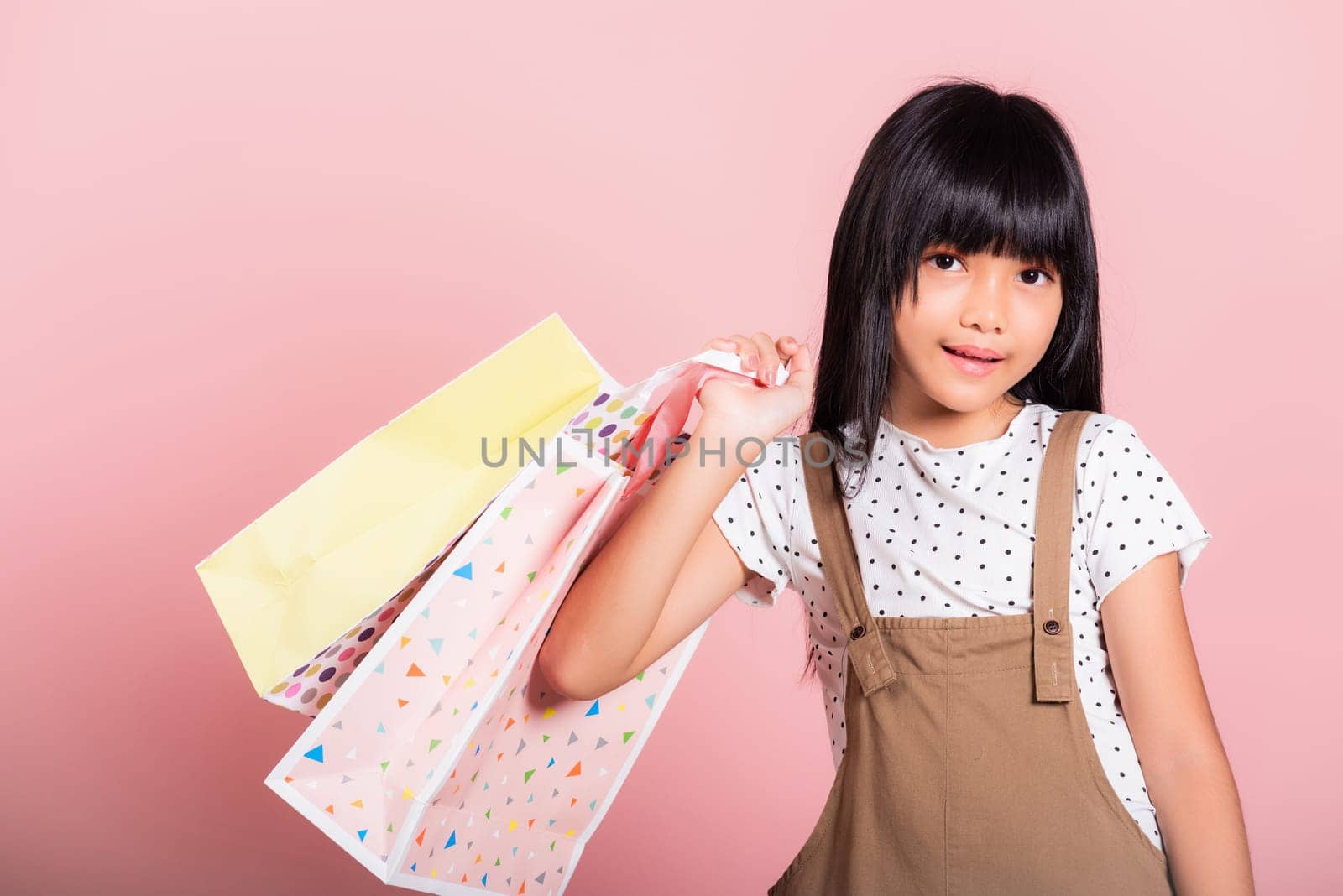 Asian little kid 10 years old smiling holding multicolor shopping bags in hands at studio shot isolated on pink background, Portrait of Happy child girl shopper lifestyle, Black friday concept