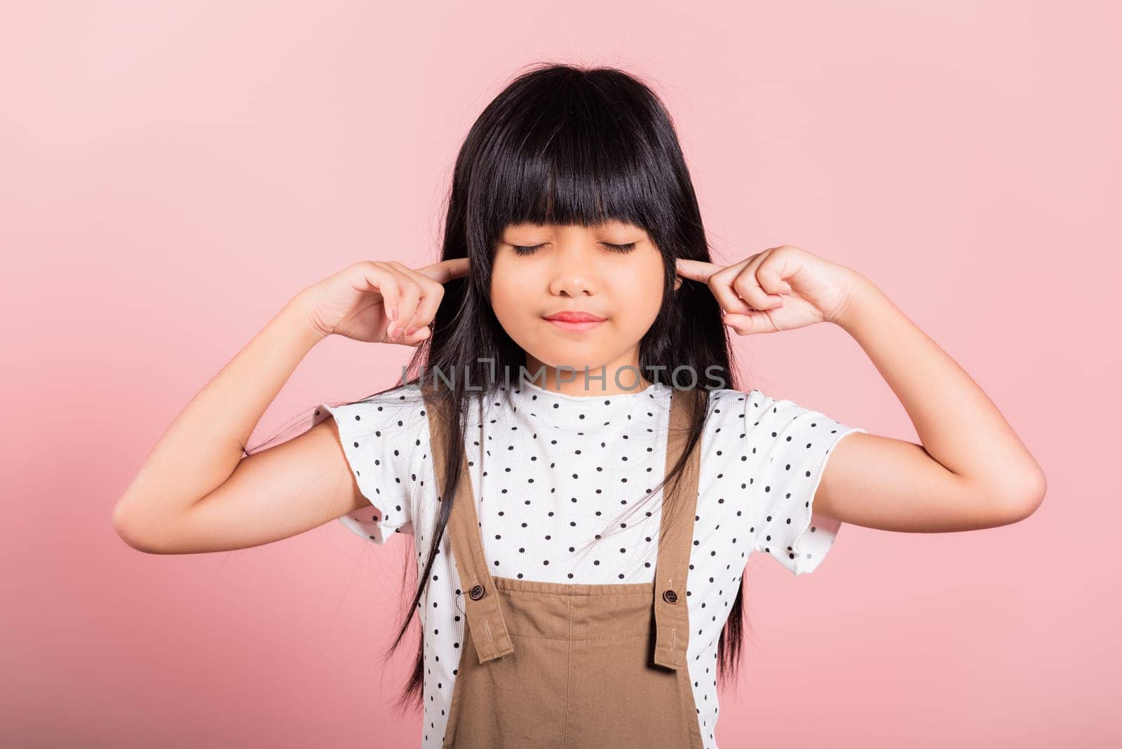 Asian little kid 10 years old Close her ears with fingers and eyes at studio shot isolated on pink background, child girl does not want to listen, Stress and noise concept