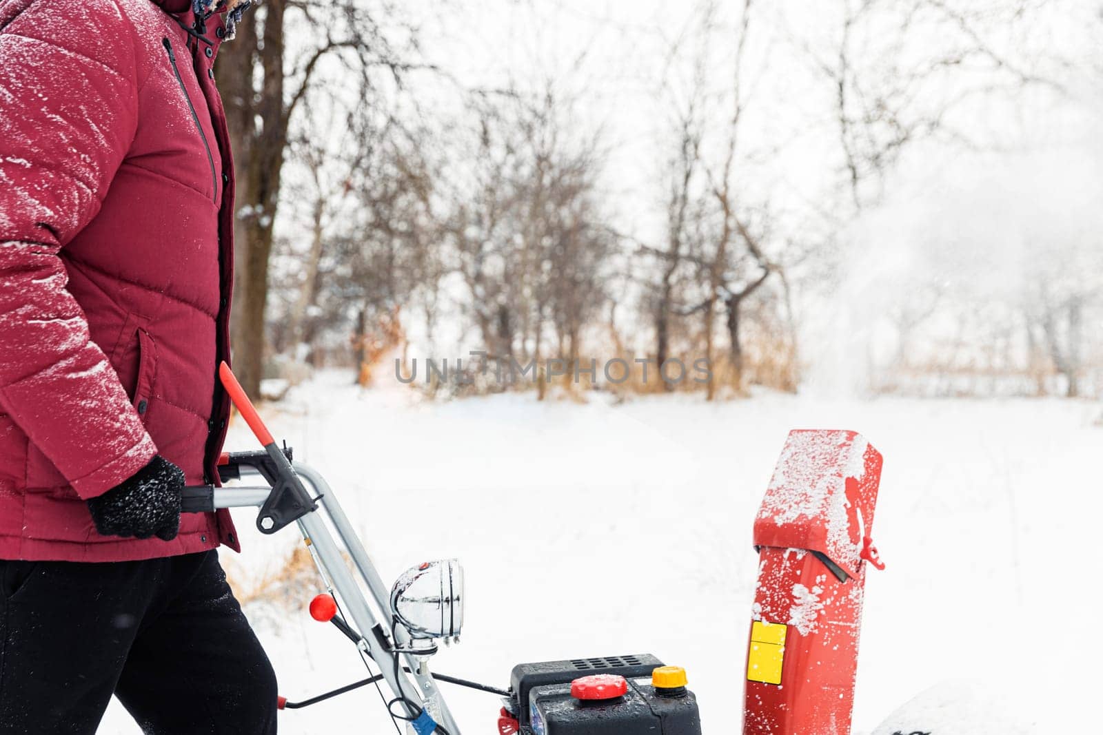 Detail of portable red snow blower powered by gasoline in action. Man outdoor using snowblower machine after snowstorm. Snow removal, thrower assistant in winter. Guy blowing snow during blizzard