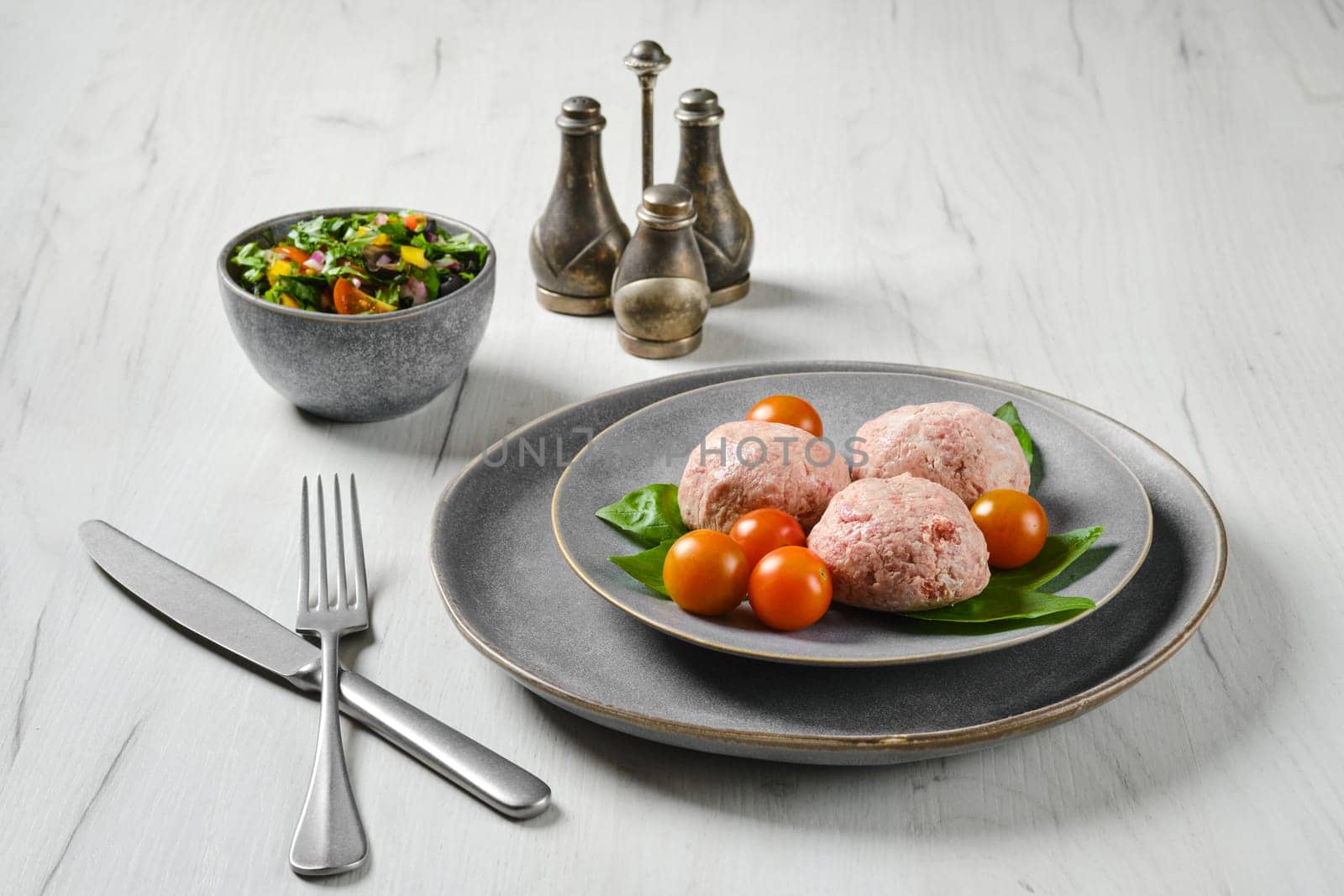 Semifinished frozen veal meatballs on a plate with basil and tomato