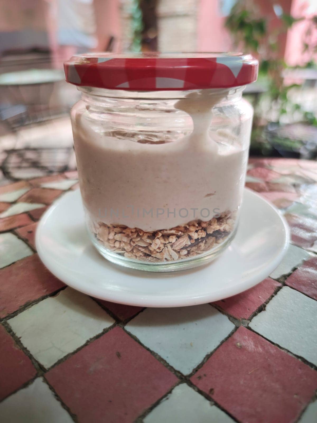 Closed Jar full of yogurt with muesli at the bottom over glazed tile mosaic table. Mediterranean style background