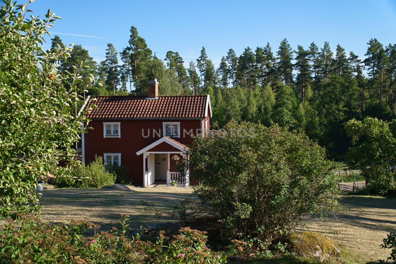 Swedish red and white tratitional house in Smalland, White fence green garden blue sky. Childhood memories from the vacations in Sweden. Nature photo from Scandinavian landscape.