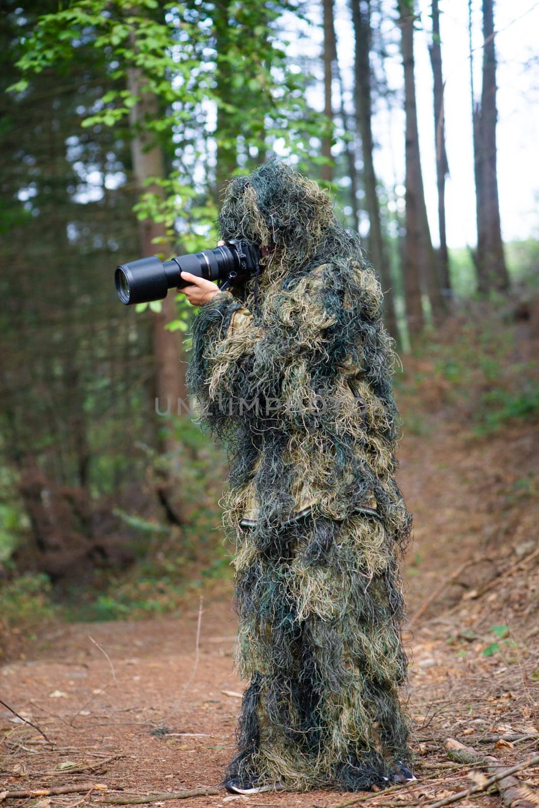 Photographer wearing camouflage clothing in the forest, wildlife animal photography with a camera and telephoto lens