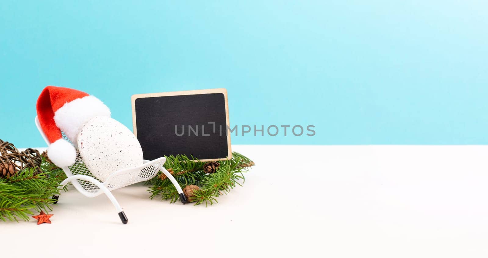 Santa Claus with a red hat sitting in a lounge chair, holiday by the sea, taking a vacation, christmas decoration with fir, cones and stars