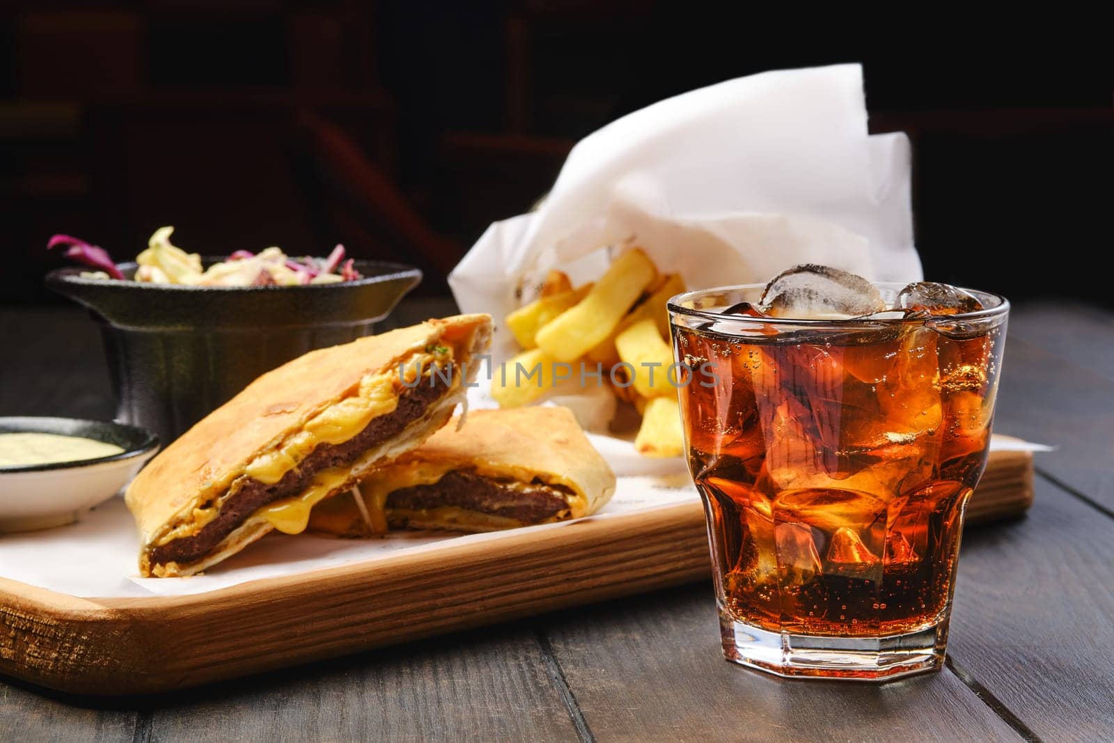 Glass of cola with ice with tortilla and fried potato on background (focus on foreground)