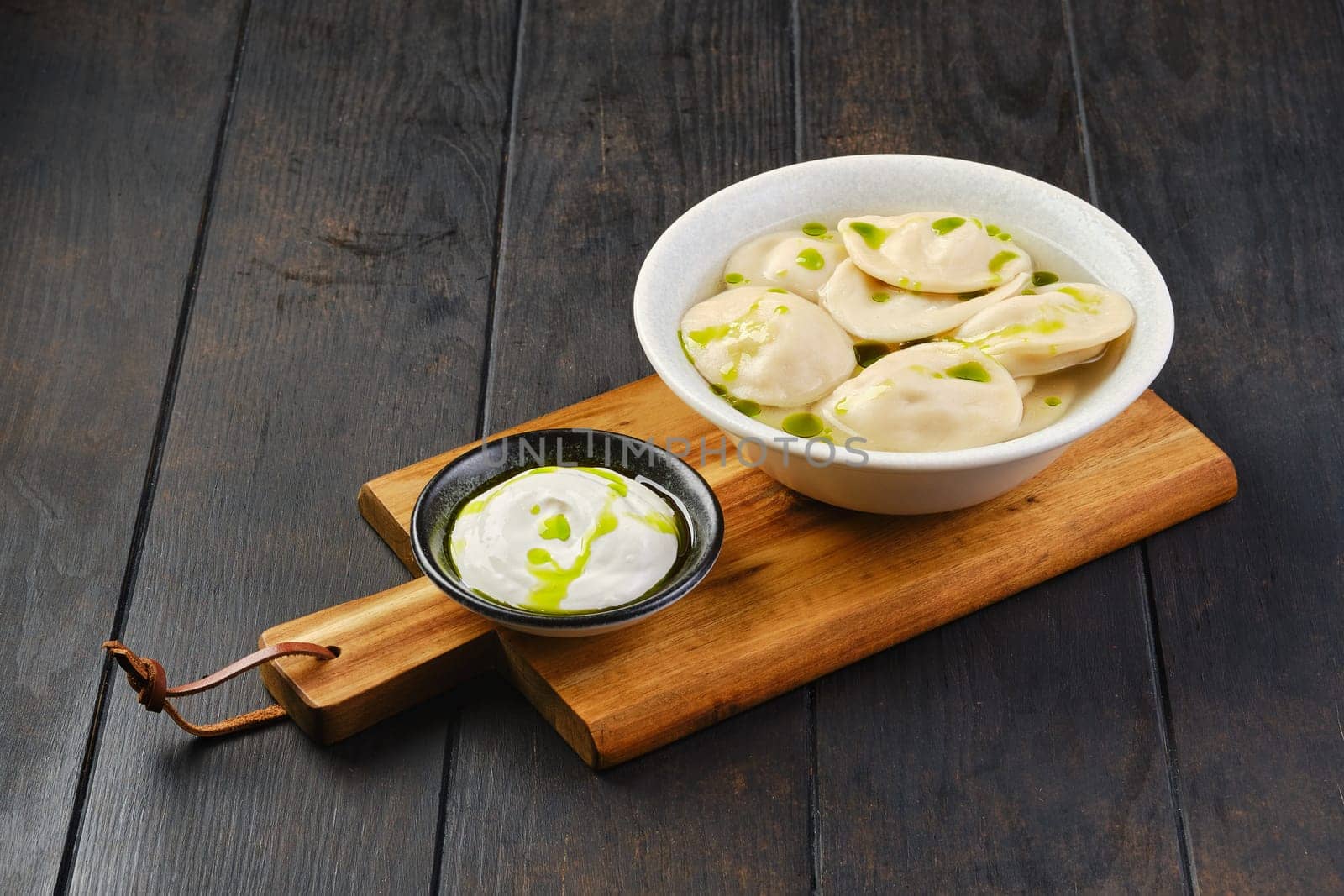 Bowl with beef pelmeni with sour cream on a wooden serving board