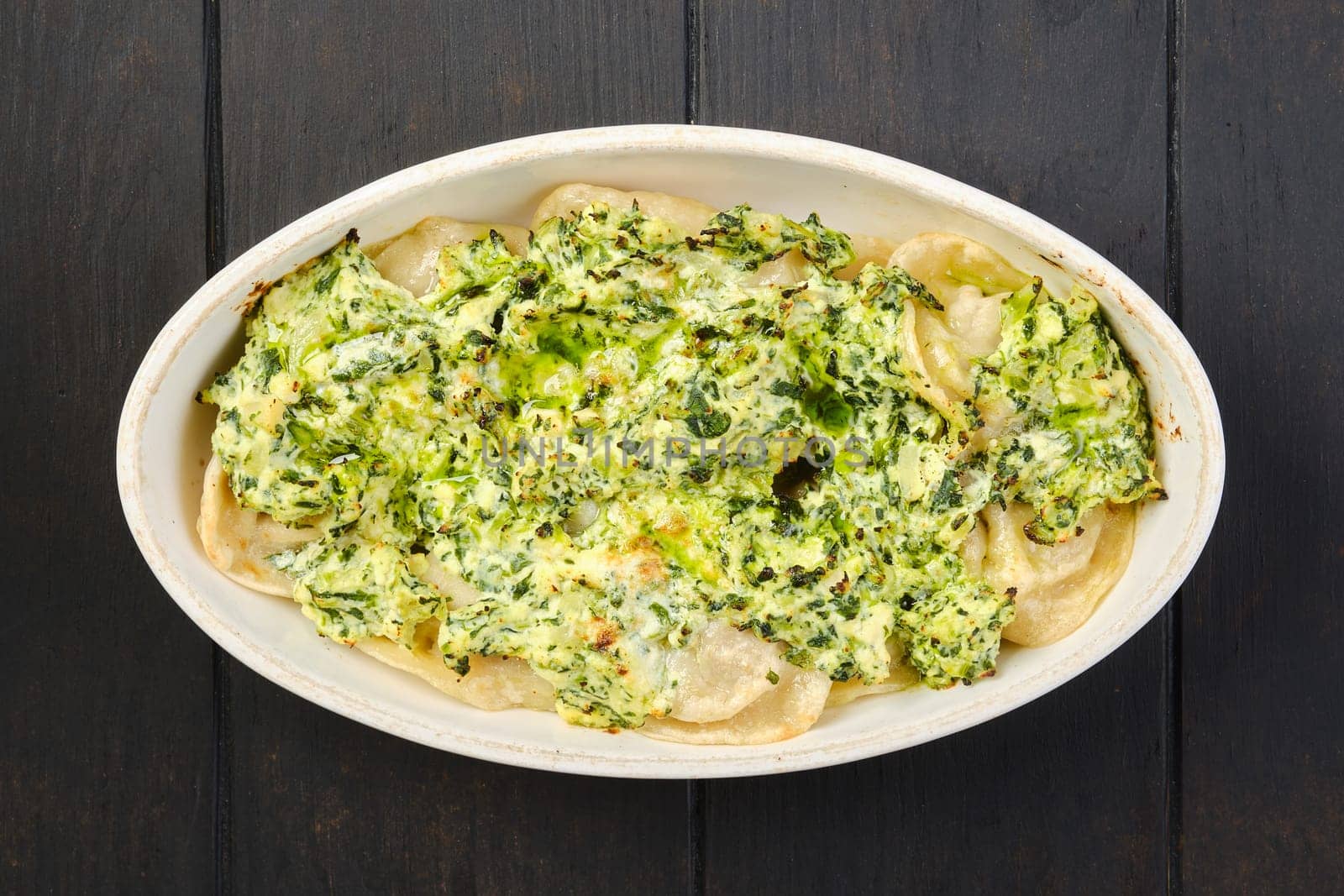 Overhead view of meat dumplings with spinach and cheese sauce baked in oven