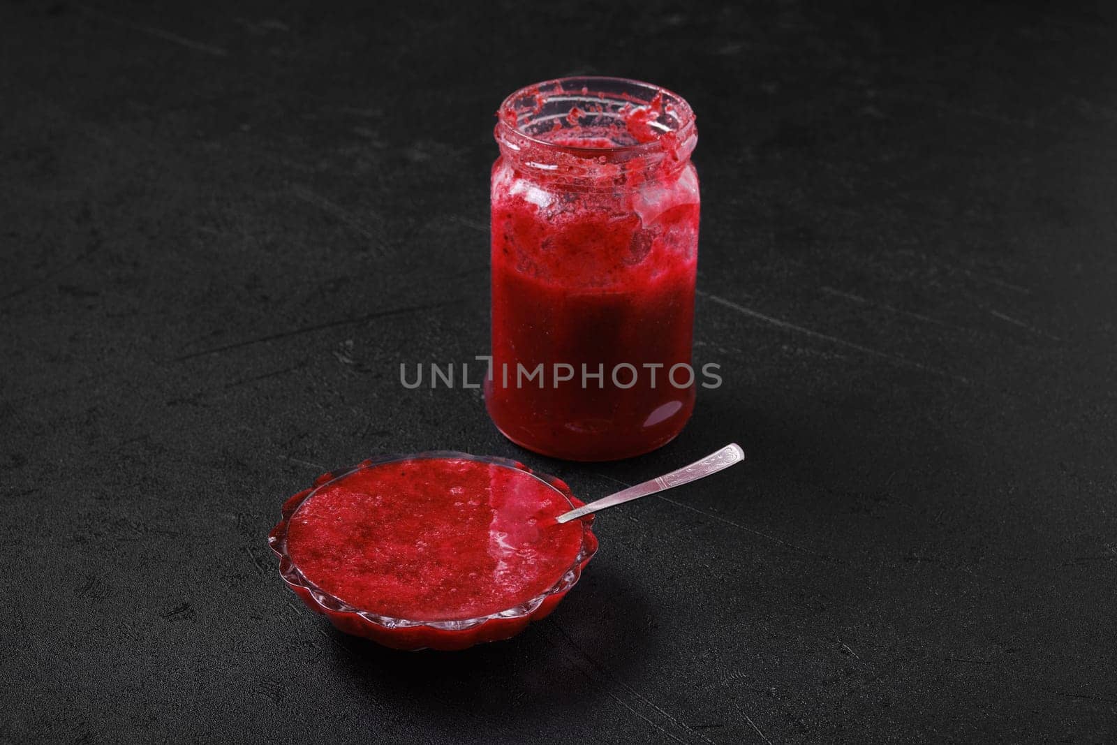 Jar and saucer with cherry jam on black background