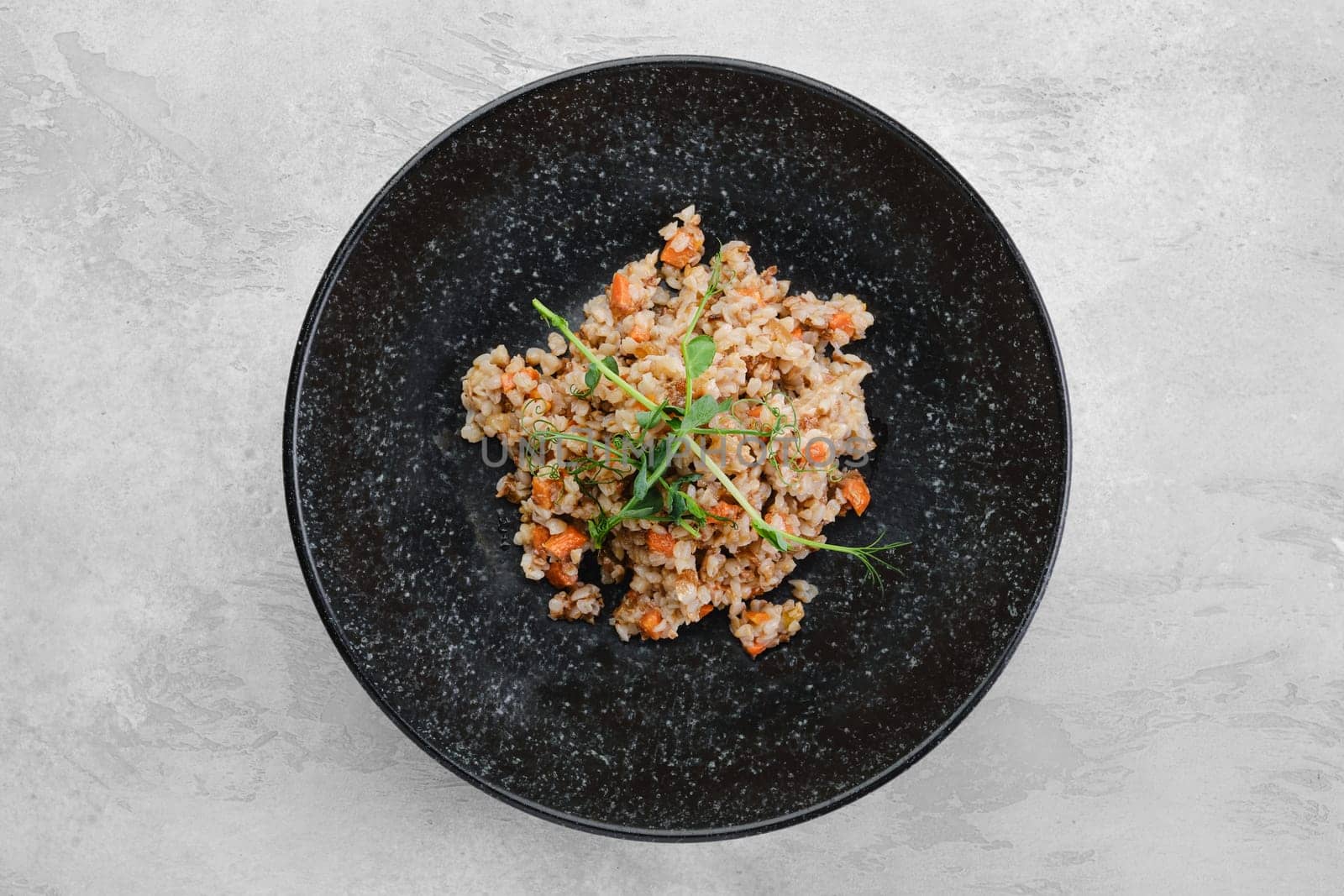 Garnish to the main dish - buckwheat porridge with slices of fried carrot on a plate, top view