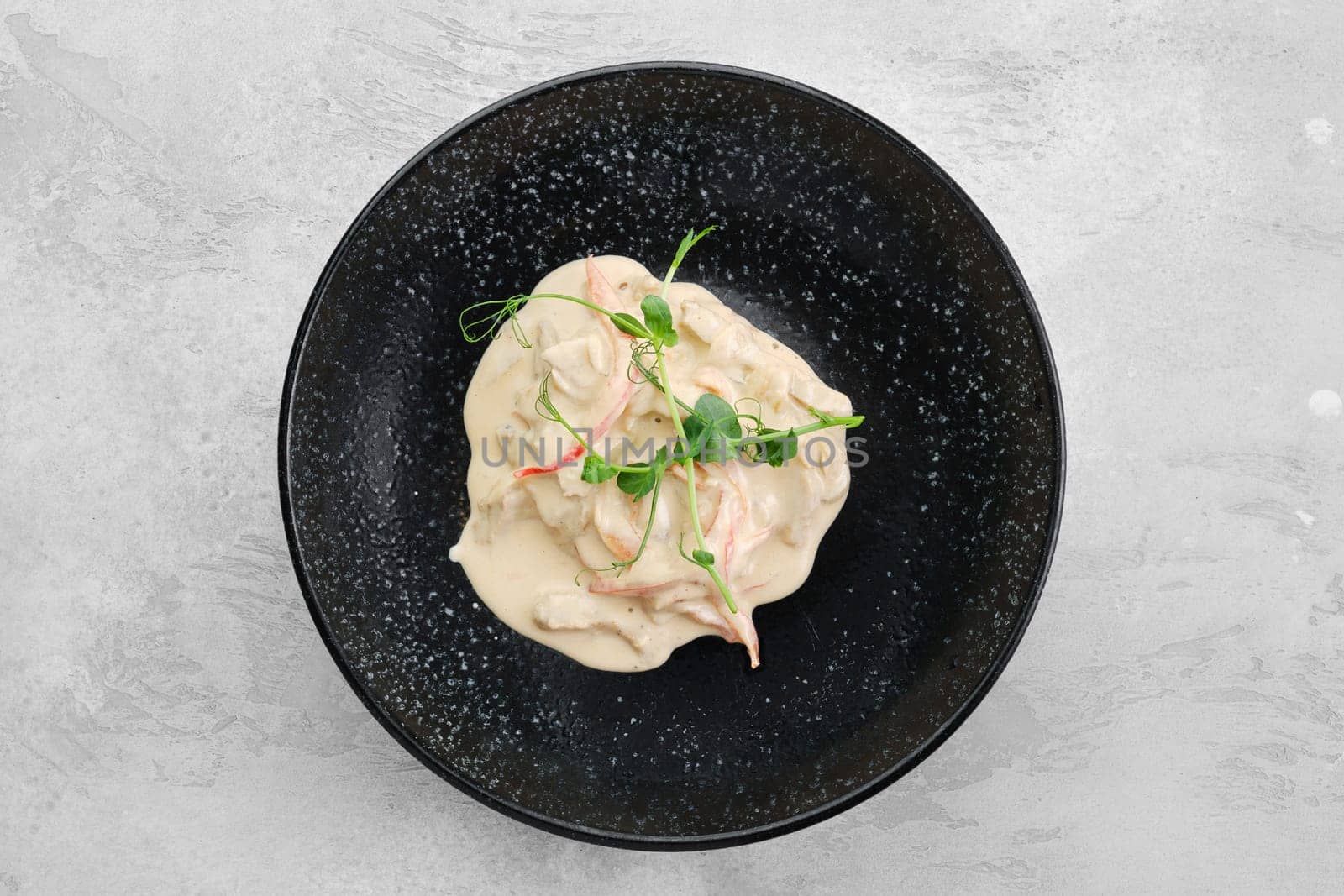 Pieces of chicken meat with bell pepper and creamy white sauce on a plate, top view