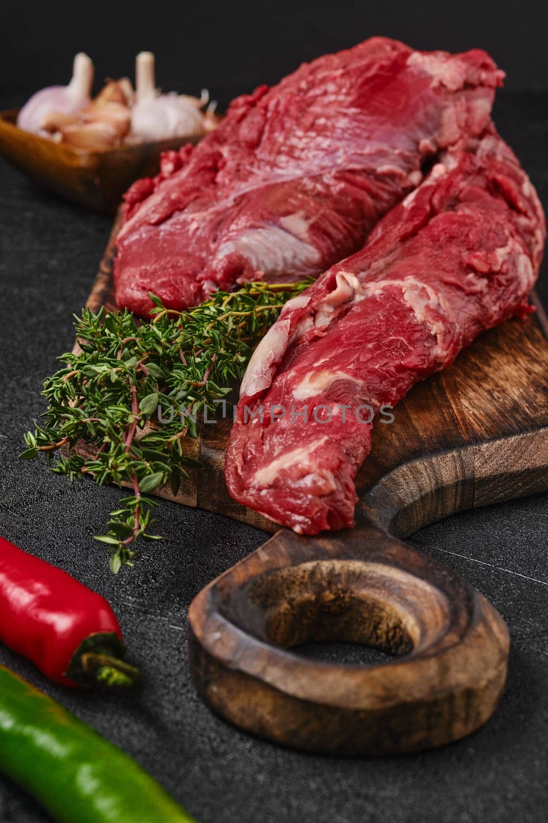 Closeup view of raw beef whole tenderloin with herbs and spice on black background
