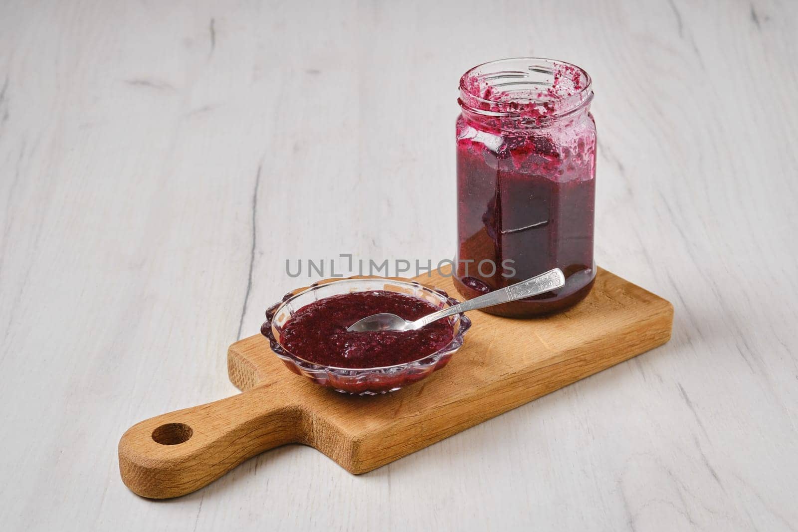 Homemade blueberry jam in a jar and saucer on wooden serving board