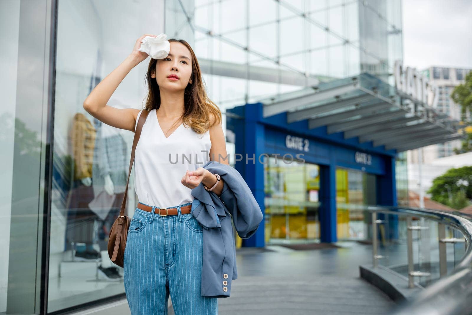 Asian beautiful business woman drying sweat her face with cloth in warm summer day hot weather, Female having sunstroke skin damage from sun UV city air pollution outdoors on street