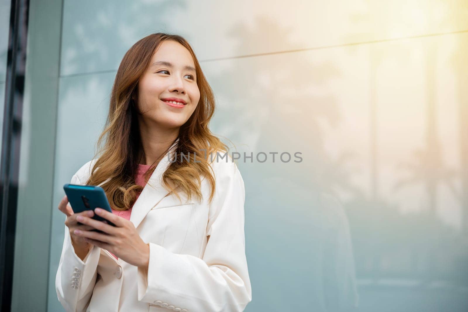 Portrait successful business woman smiling holding smartphone using app chat online in morning, Asian businesswoman typing text on mobile phone standing outdoors street front building near office