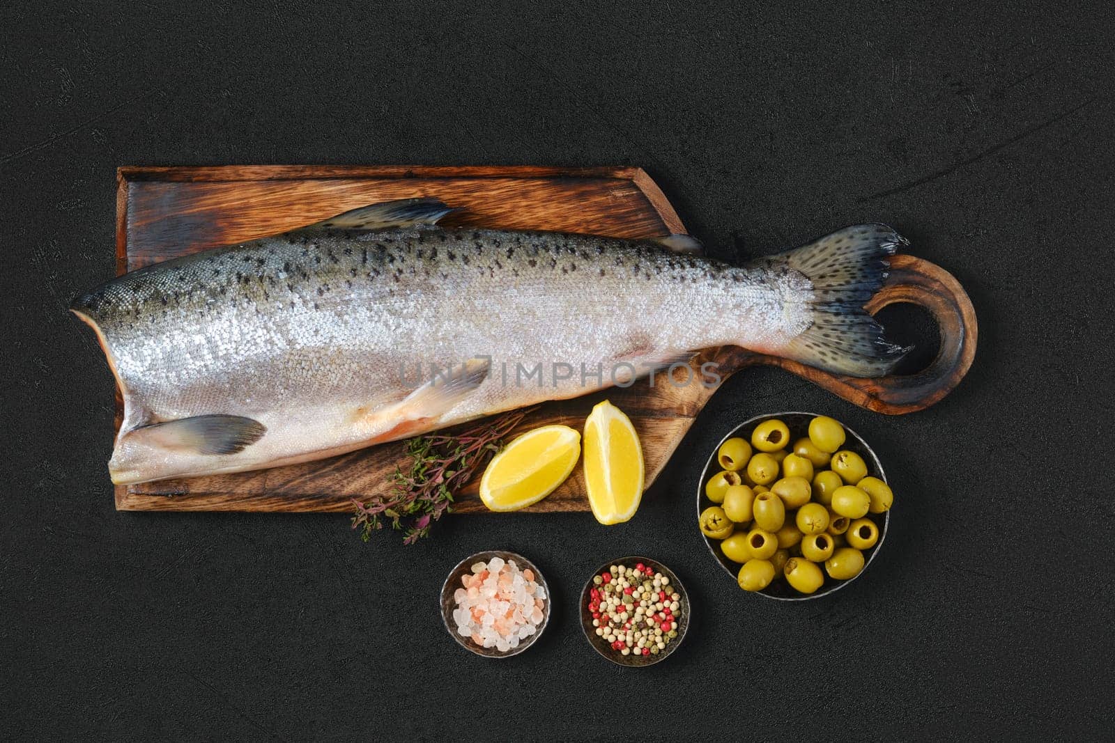 Headless fresh chinook on wooden cutting board with spice and lemon, top view