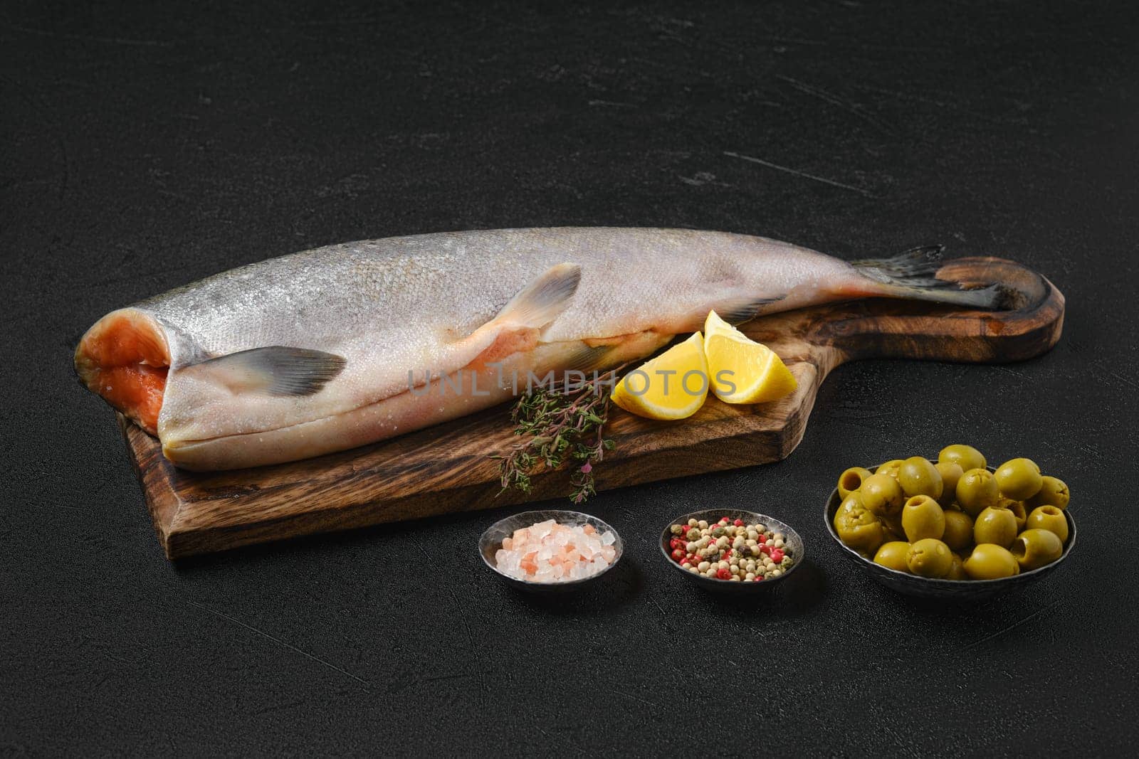 Headless fresh chinook on wooden cutting board with spice and lemon