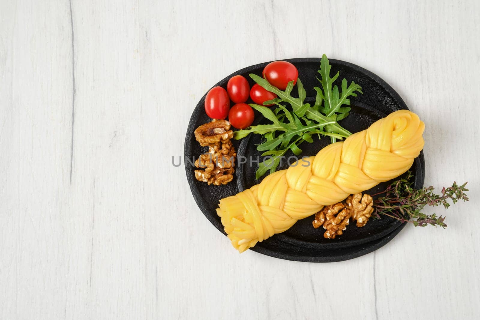 Smoked braided cheese with walnuts and tomatoes on a plate, top view