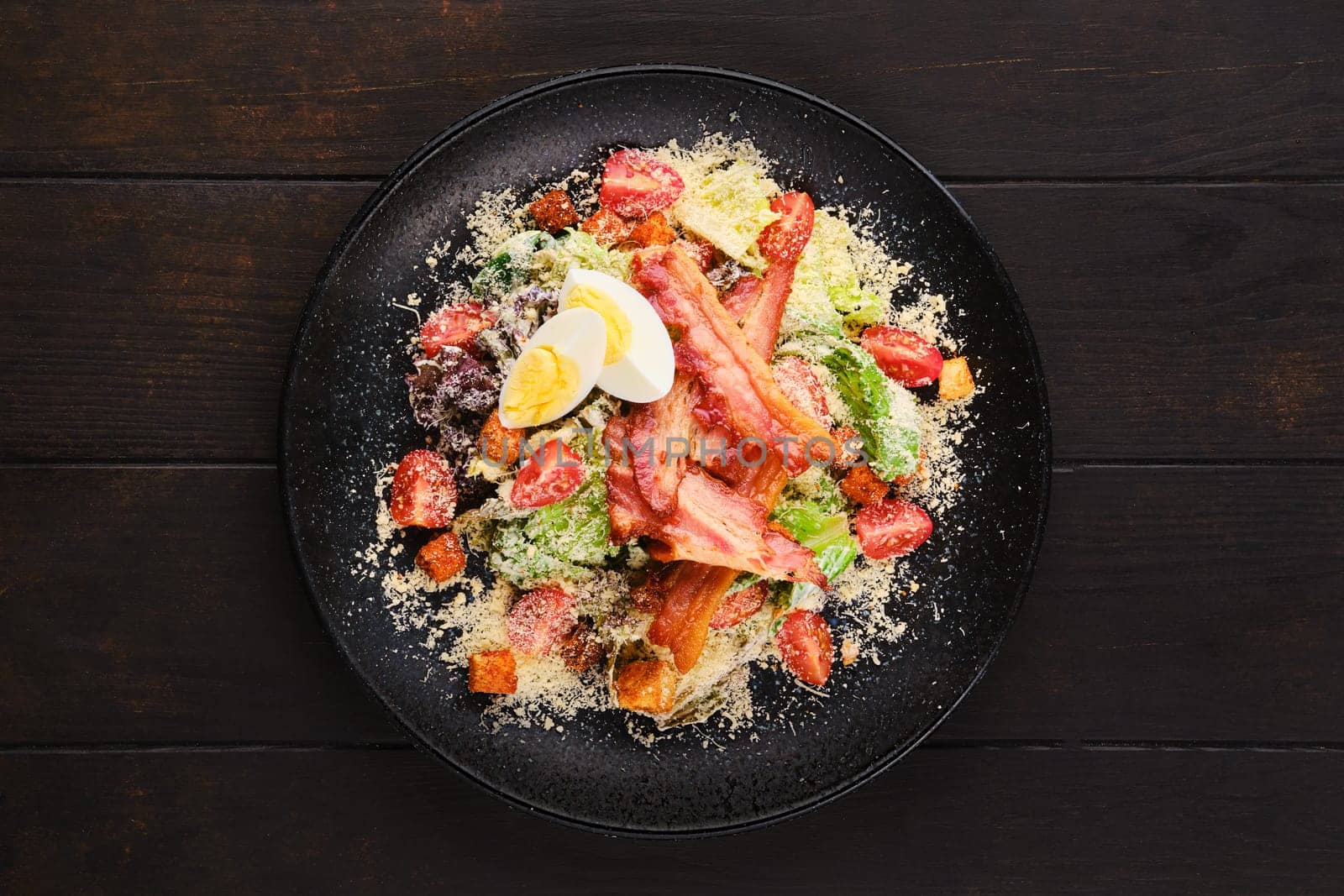 Salad with bacon, egg, fresh vegetables, croutons and grated cheese, top view