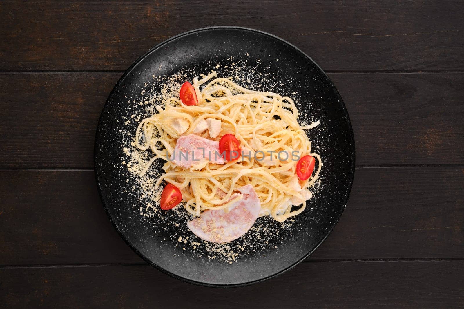 Spaghetti with ham and tomatoes sprinkled with grated parmesan, top view
