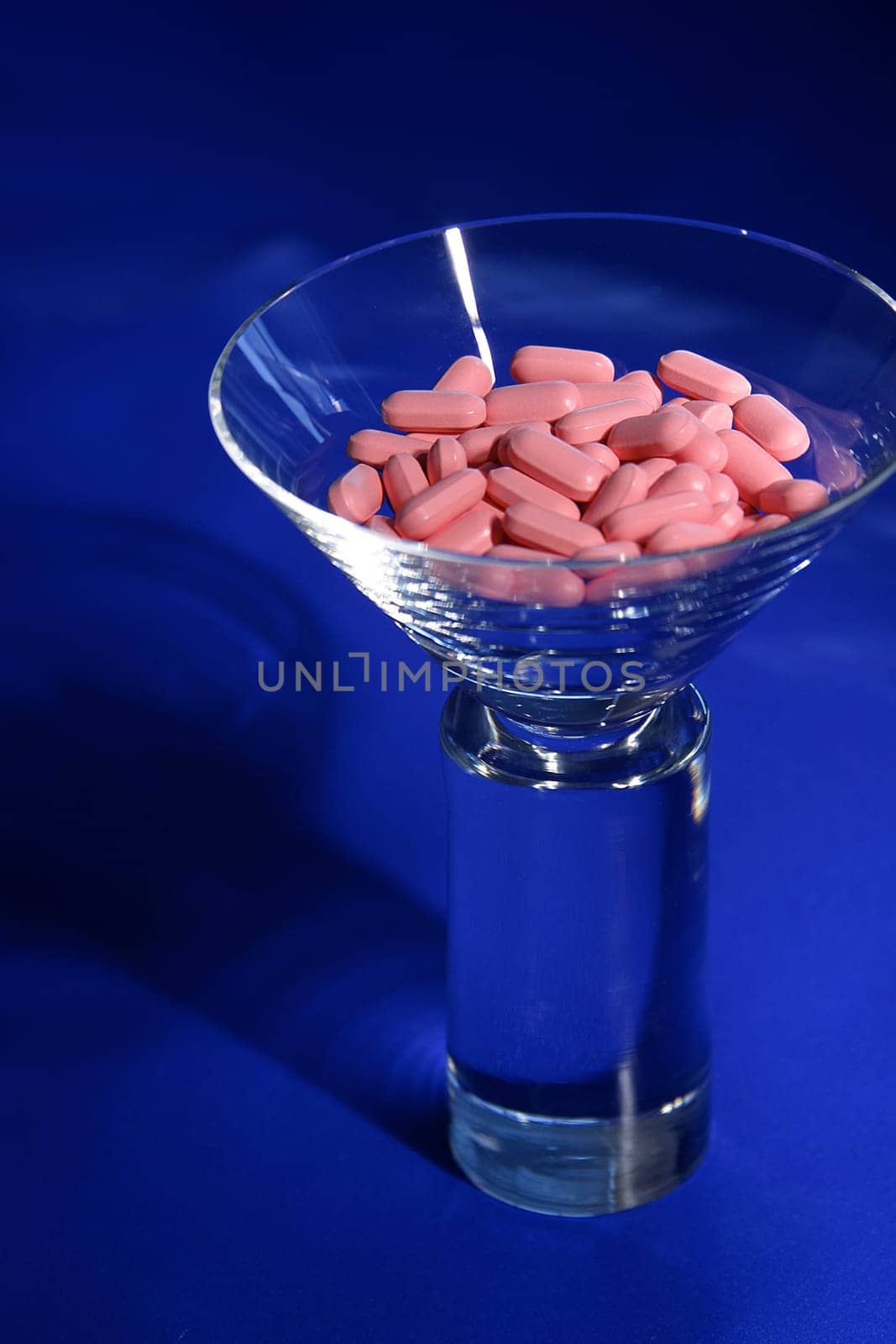 A martini glass filled with pink vitamins on a blue background