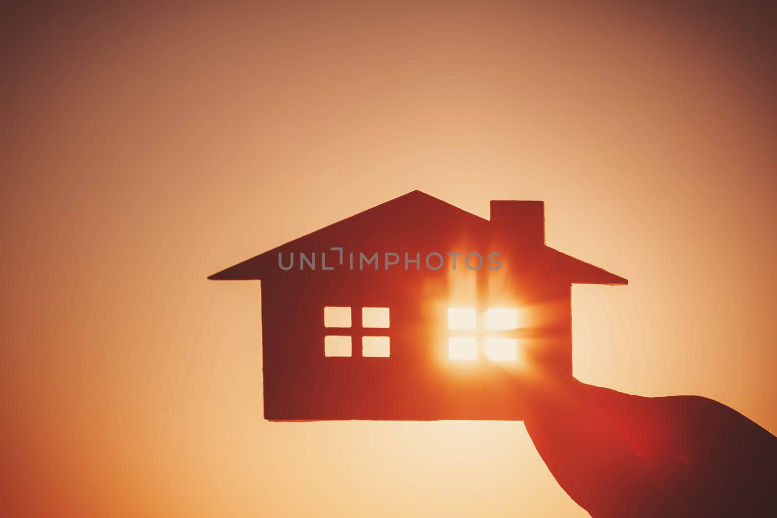 Woman's hand holding a model of a house on sunset evening. Concept of buying or selling a new appartment.