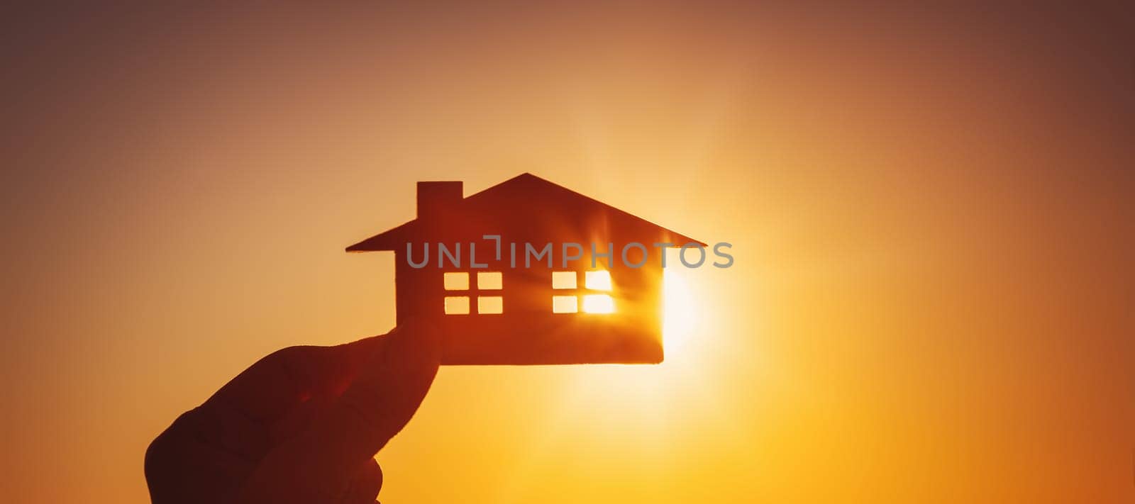 Woman's hand holding a model of a house on sunset evening. Concept of buying or selling a new appartment.