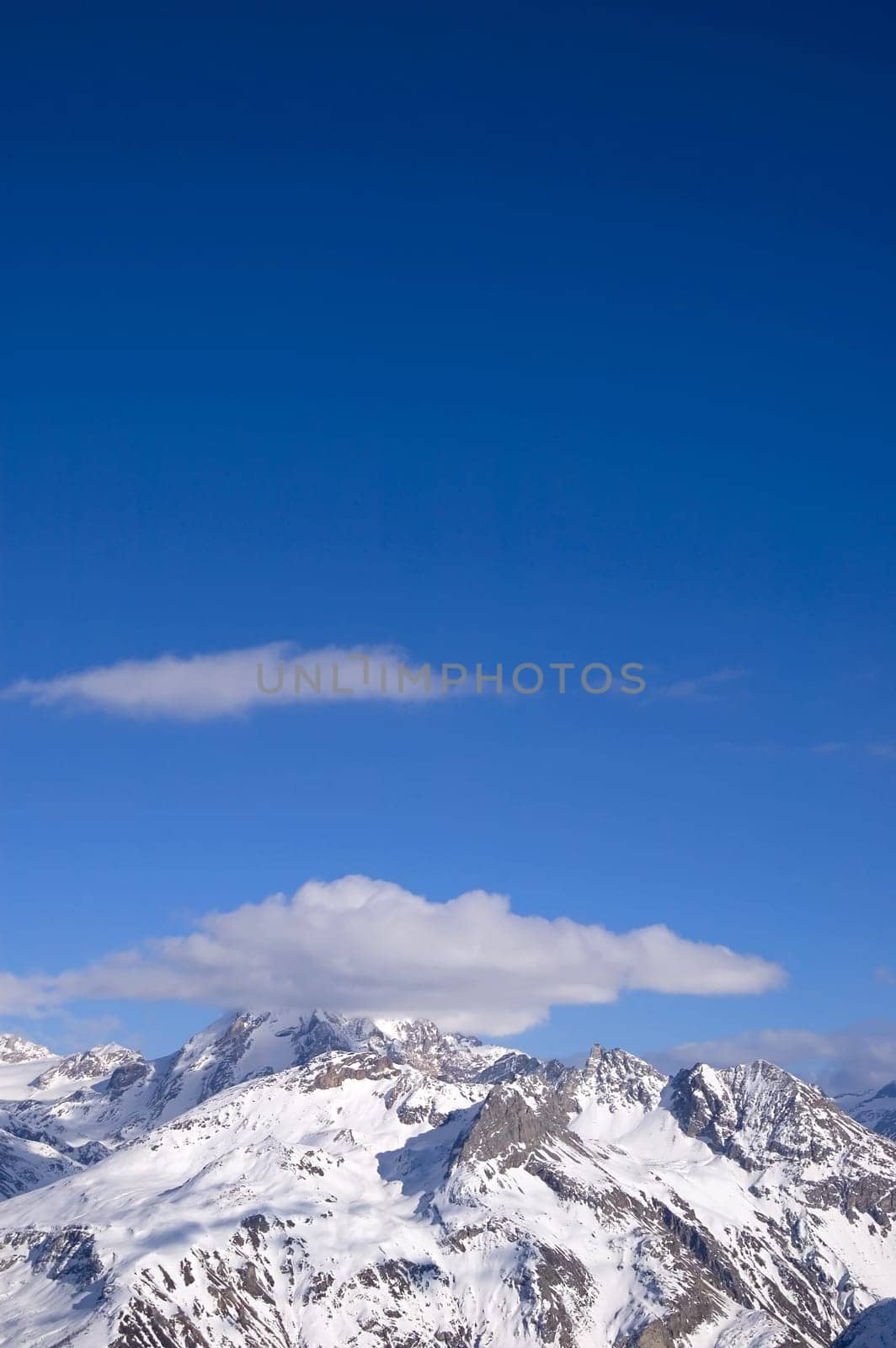 snowed peak of a mountain surrounded by small cloud, a lot of blue for copy-space