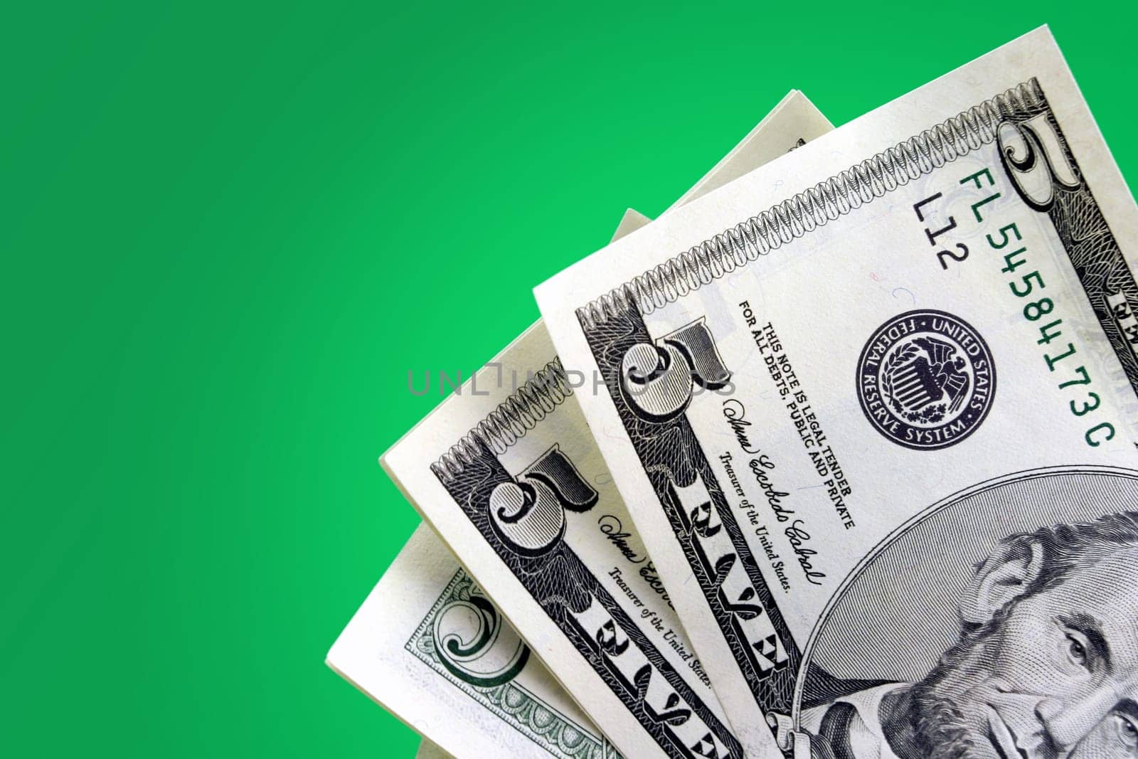 Closeup of five dollar bills against green gradient background.
