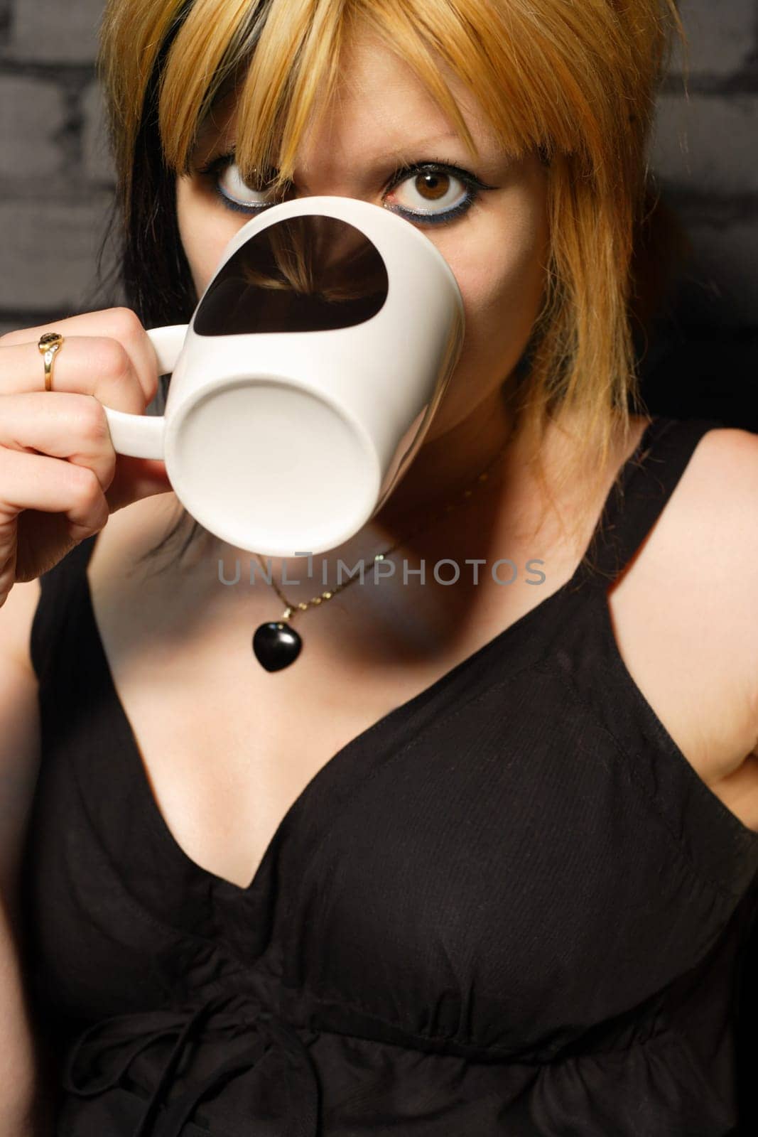 Female drinking coffee against the black brick wall of a urban café.
