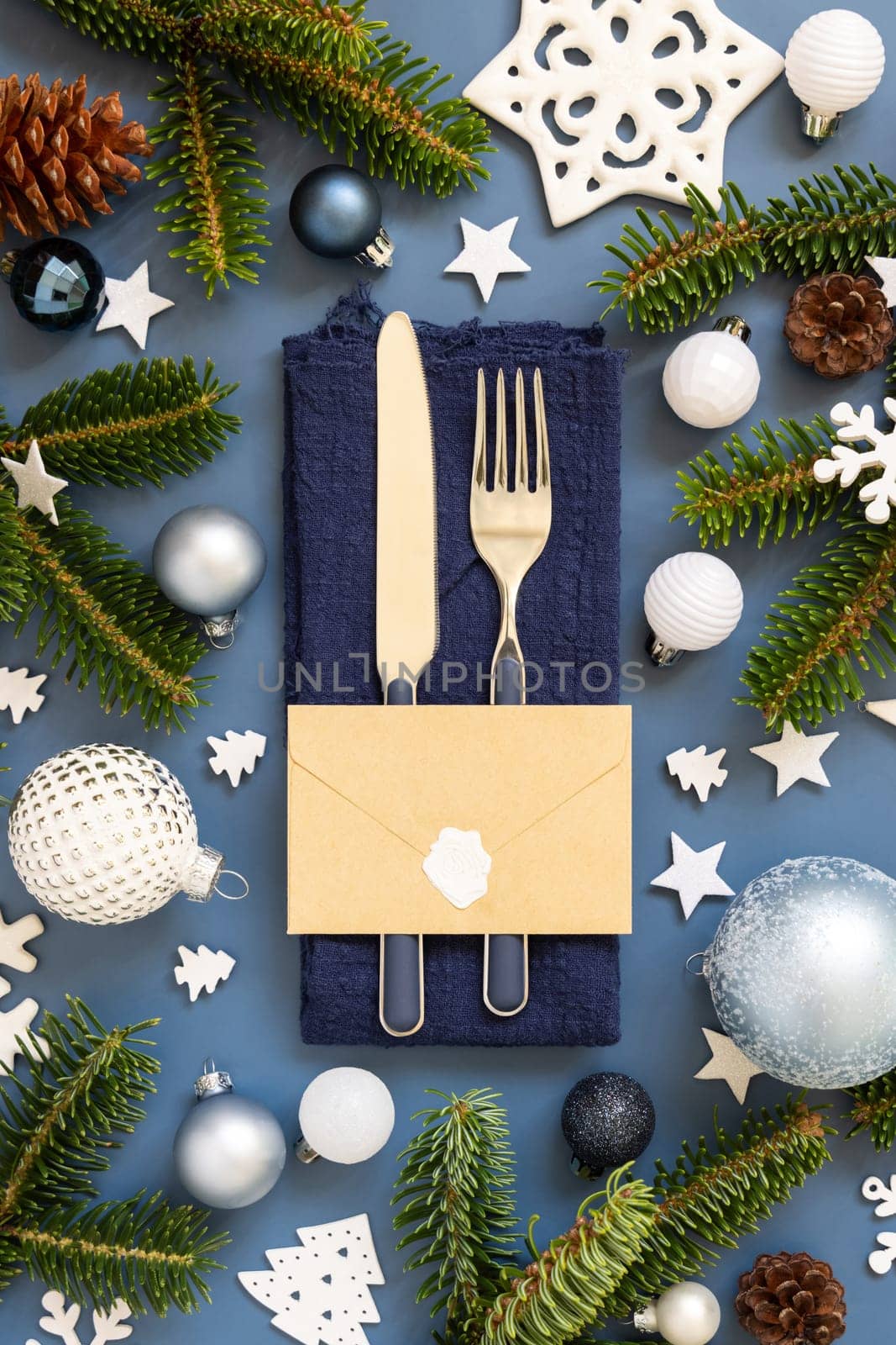 Blue and white Christmas table setting with envelope near decorations and fir tree branches top view. Winter table with fork, knife and plate. Winter New Year or Christmas dinner atmosphere