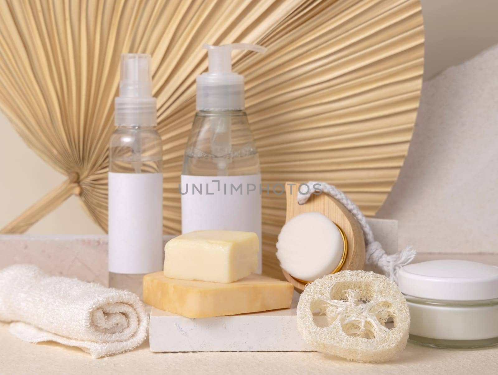 Small bottles and handmade soap bars on stone against dry beige palm leaf close up, label mockup. Skincare beauty products, cream or lotion. Natural organic cosmetics. Minimal eco friendly composition..
