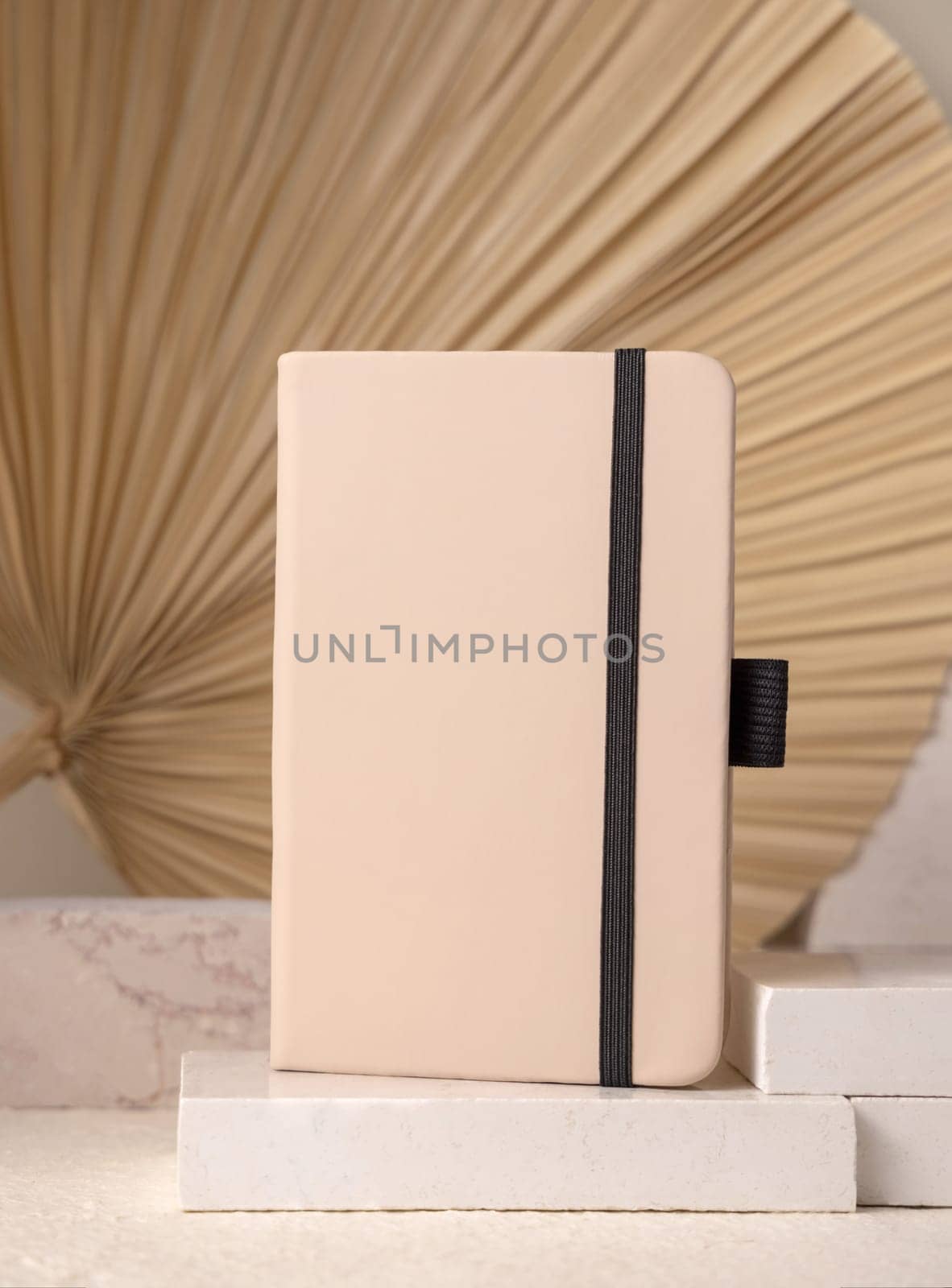 Hardcover texbook on beige stone against dry beige palm leaf close up, mockup. Boho scene with blank notebook Bohemian or close to nature concept. Minimal composition.